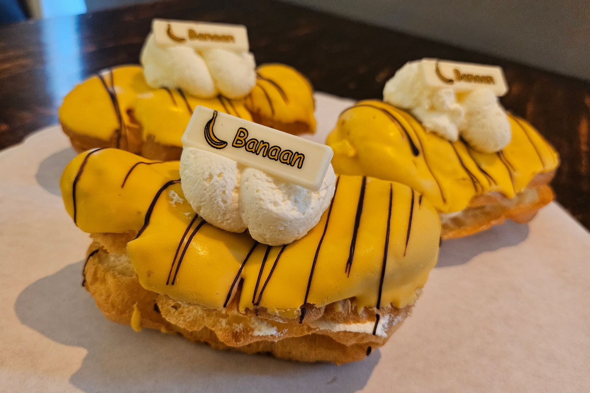 Drie met gele glazuur bedekte roomgebakjes, gegarneerd met stukjes witte chocolade en besprenkeld met chocoladesaus.
