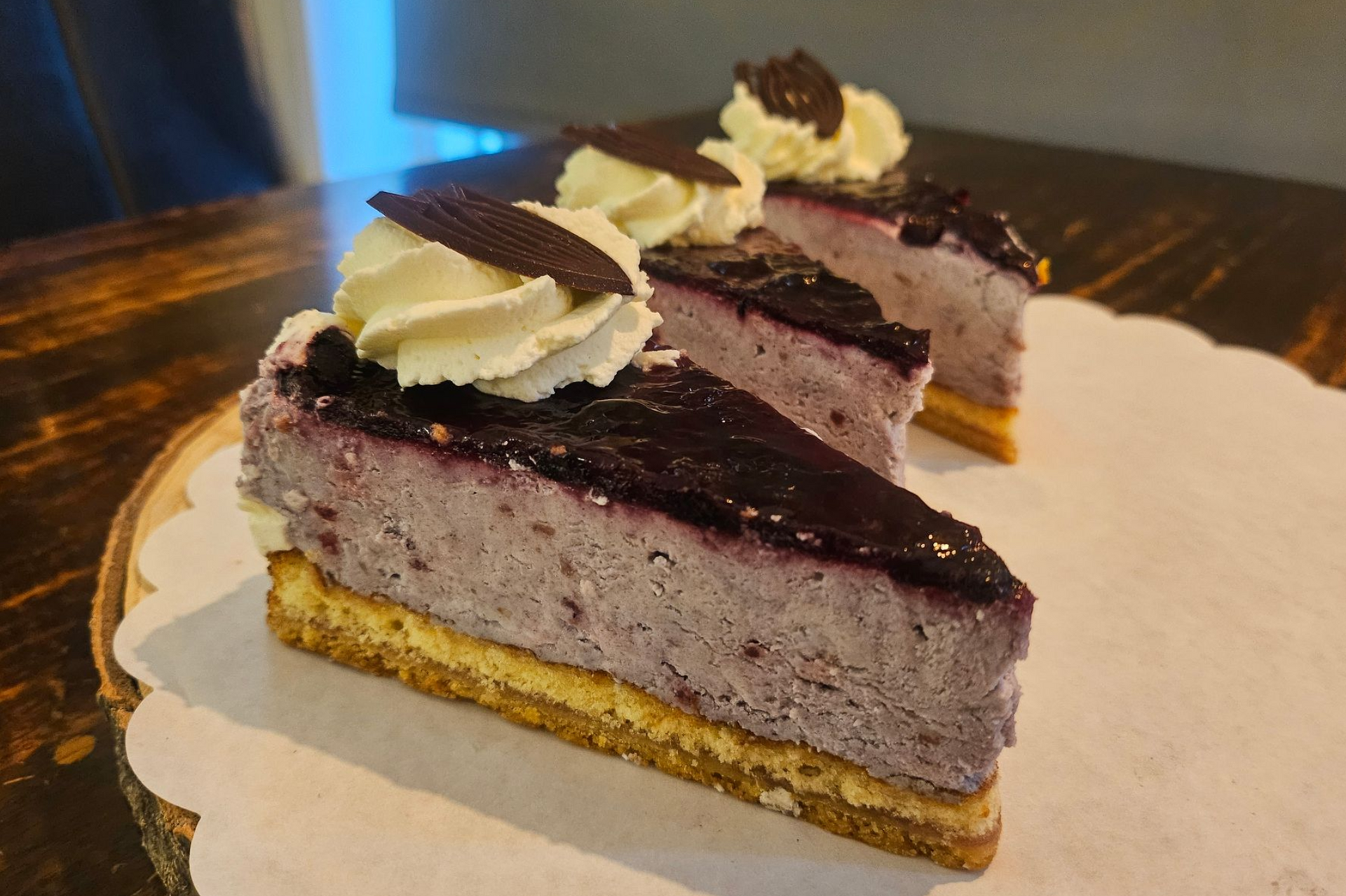 Twee plakken bosbessencheesecake met slagroom en chocoladeschilfers.