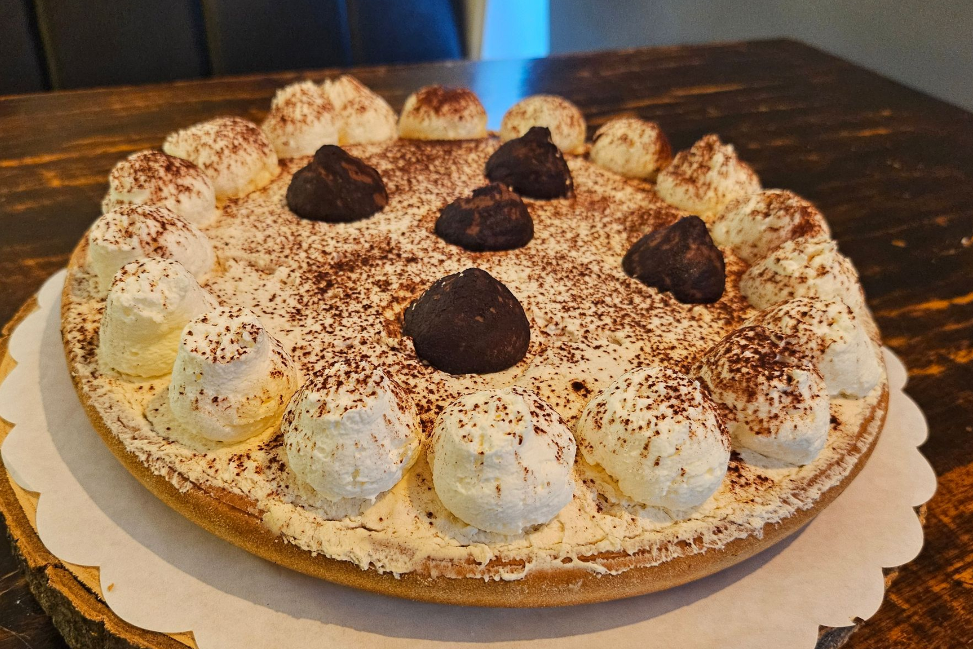 Een ronde taart, versierd met slagroomkrullen, chocoladeschaafsel en vier pure chocoladetruffels.