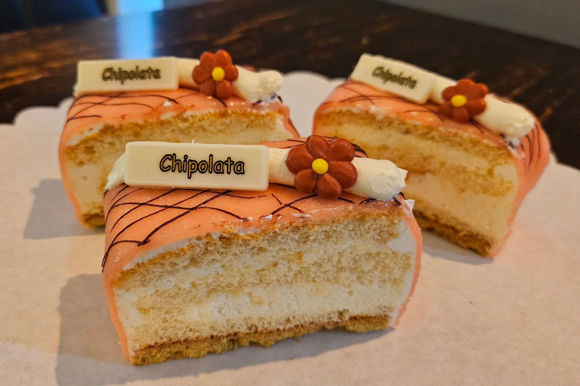Drie rechthoekige plakken met witte cremé, dunne chocoladelijnen en een bloemversiering.