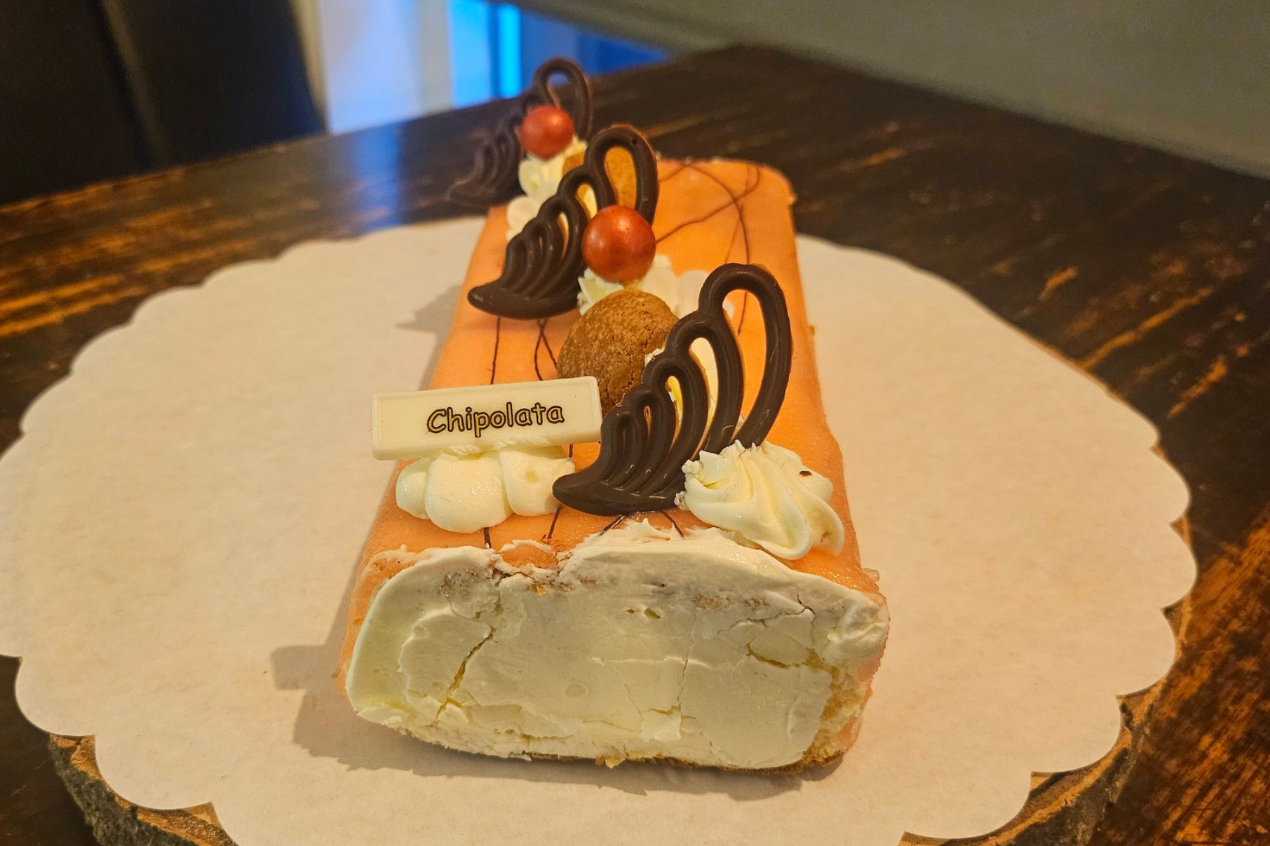 Een rechthoekige cakerol versierd met chocoladekrullen en witte crème.