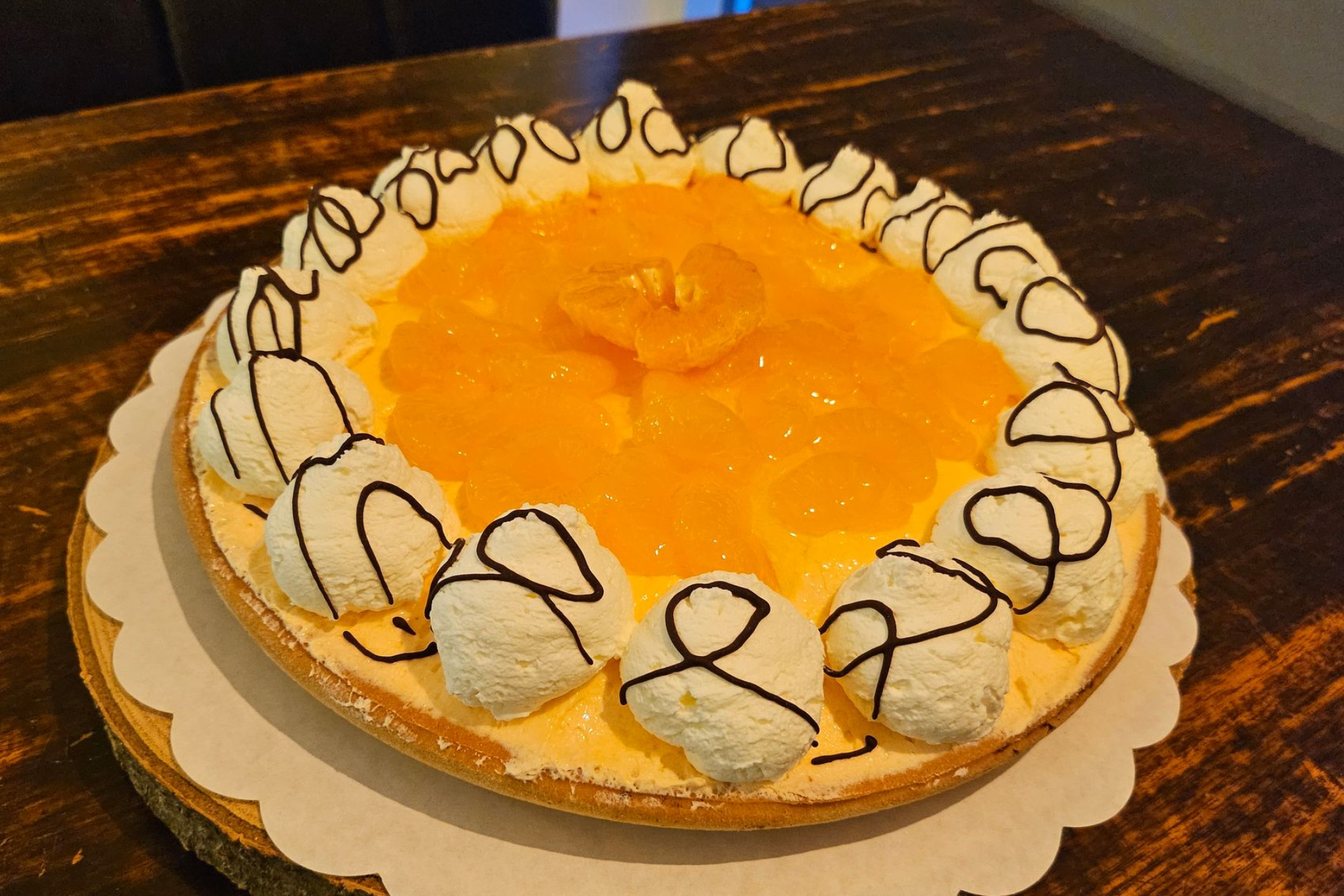 Een vruchtentaart, gegarneerd met sinaasappelschijfjes, omringd door toefjes slagroom en besprenkeld met pure chocolade.