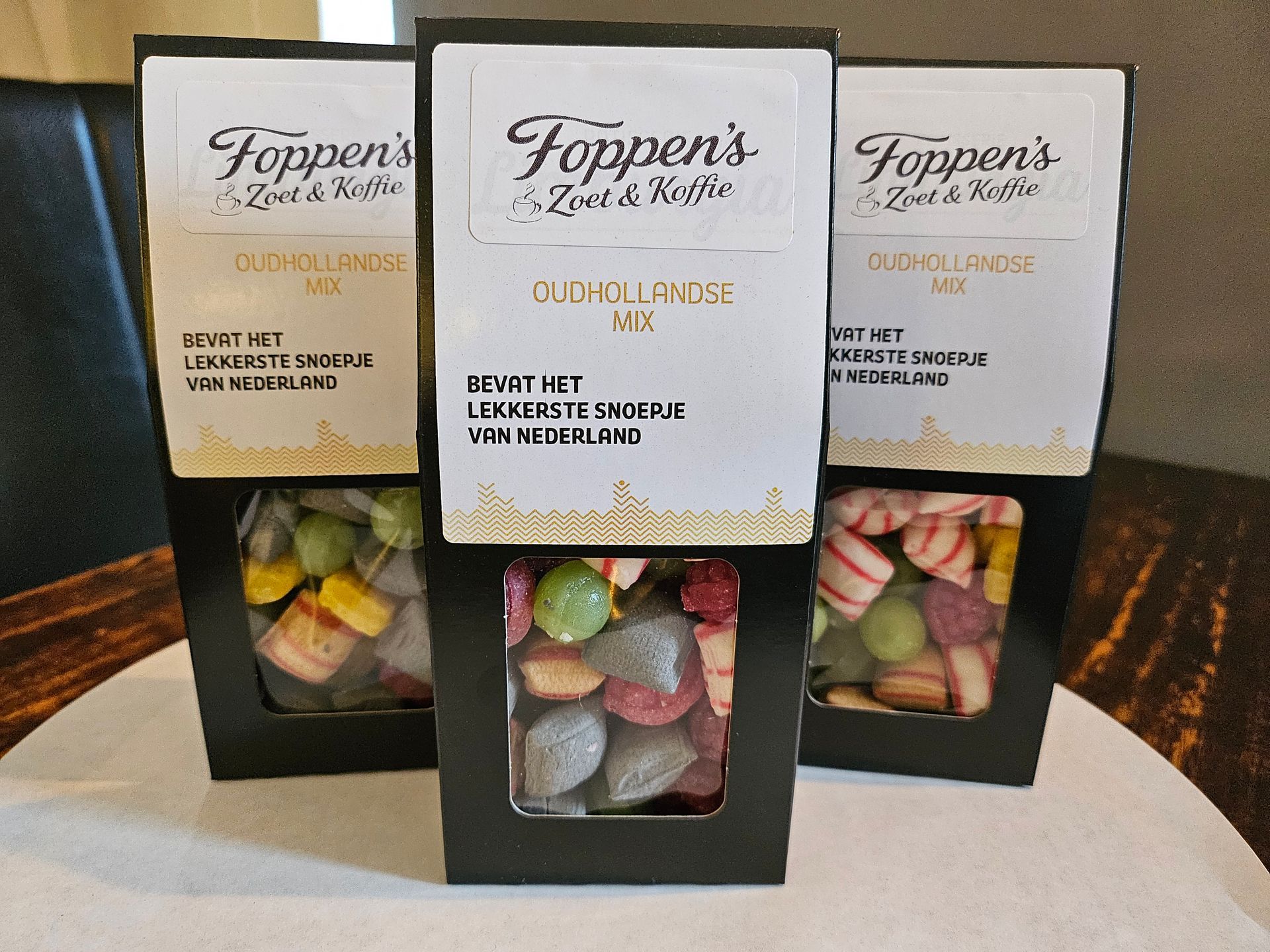 Op een tafel liggen drie pakjes snoepjes, in zwarte, gouden en witte dozen, met daarin verschillende soorten snoepgoed.