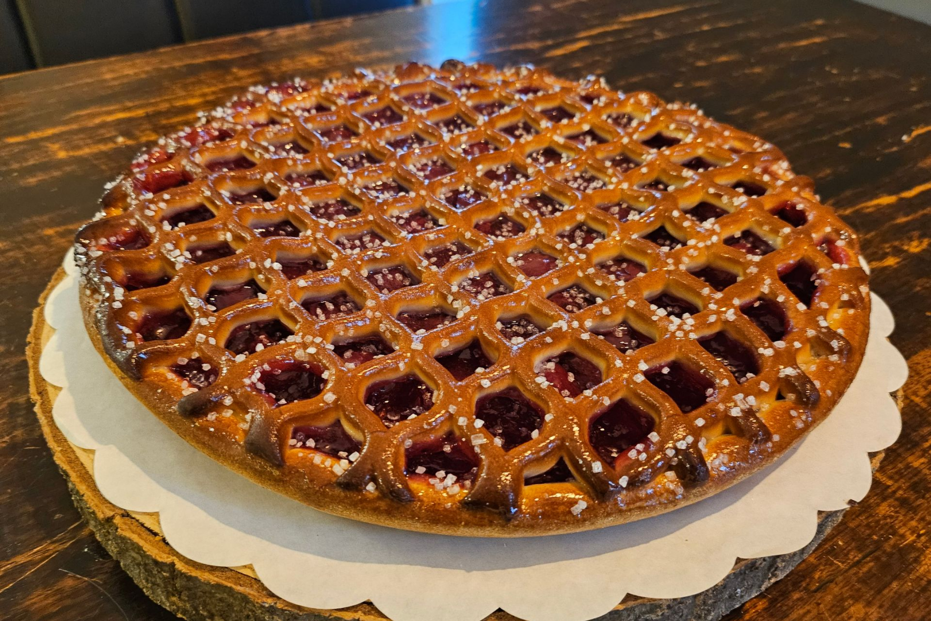 Een bessentaart met een rastervormig dak en een goudbruine korst, bestrooid met grove suiker.
