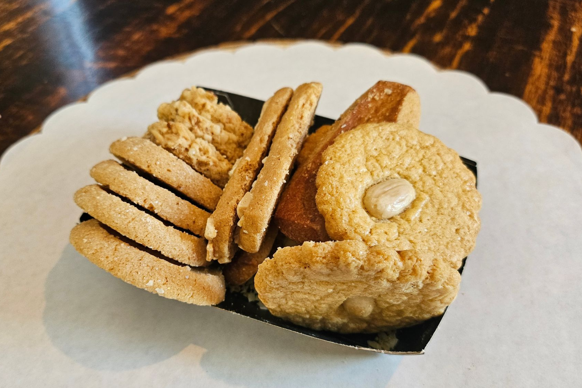 In een zwart papieren bakje liggen verschillende goudbruine koekjes, waaronder ronde, gegolfde en rechthoekige exemplaren.