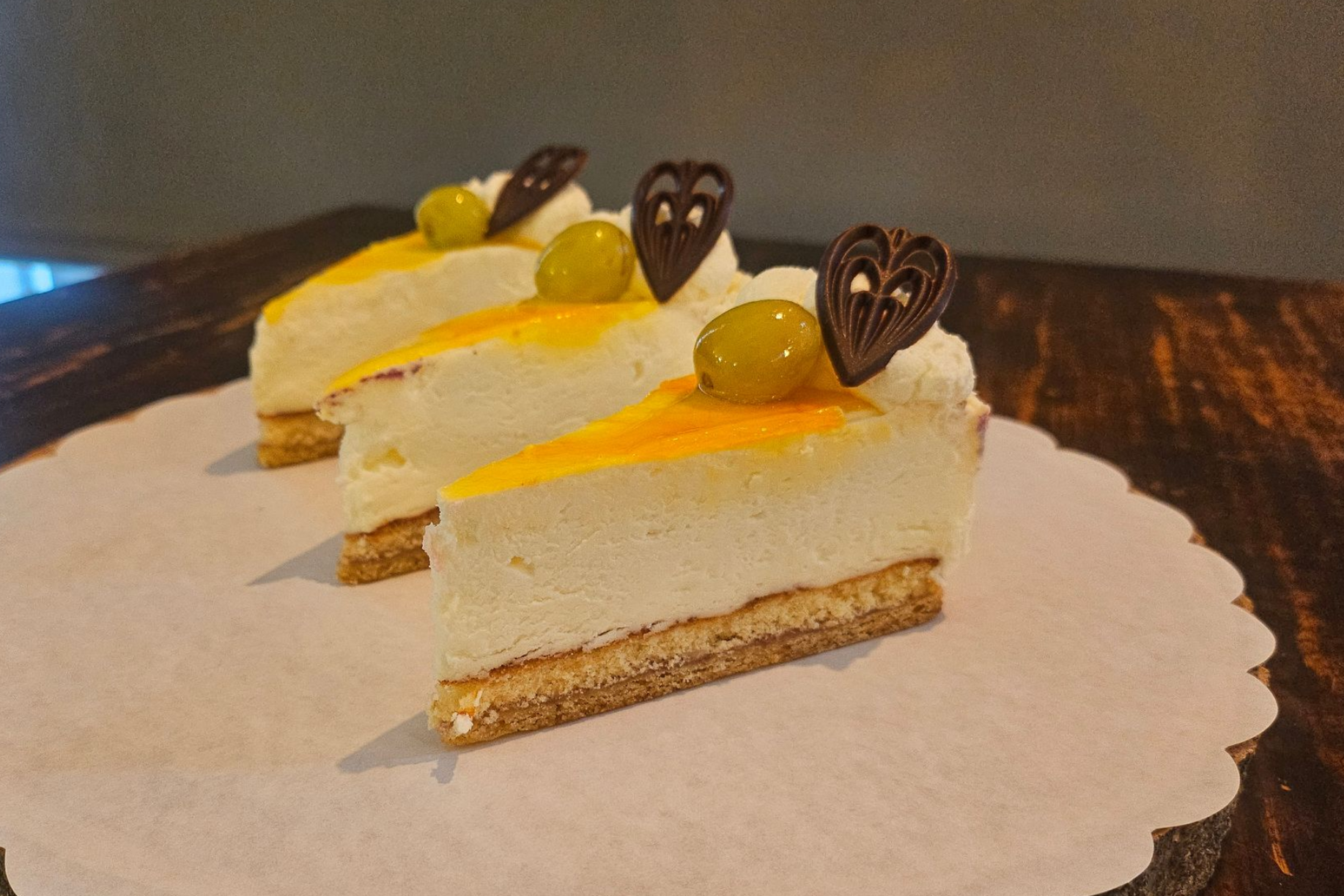 Drie driehoekige plakken romige cheesecake, bedekt met gele glazuur, druiven en hartvormige chocolade.
