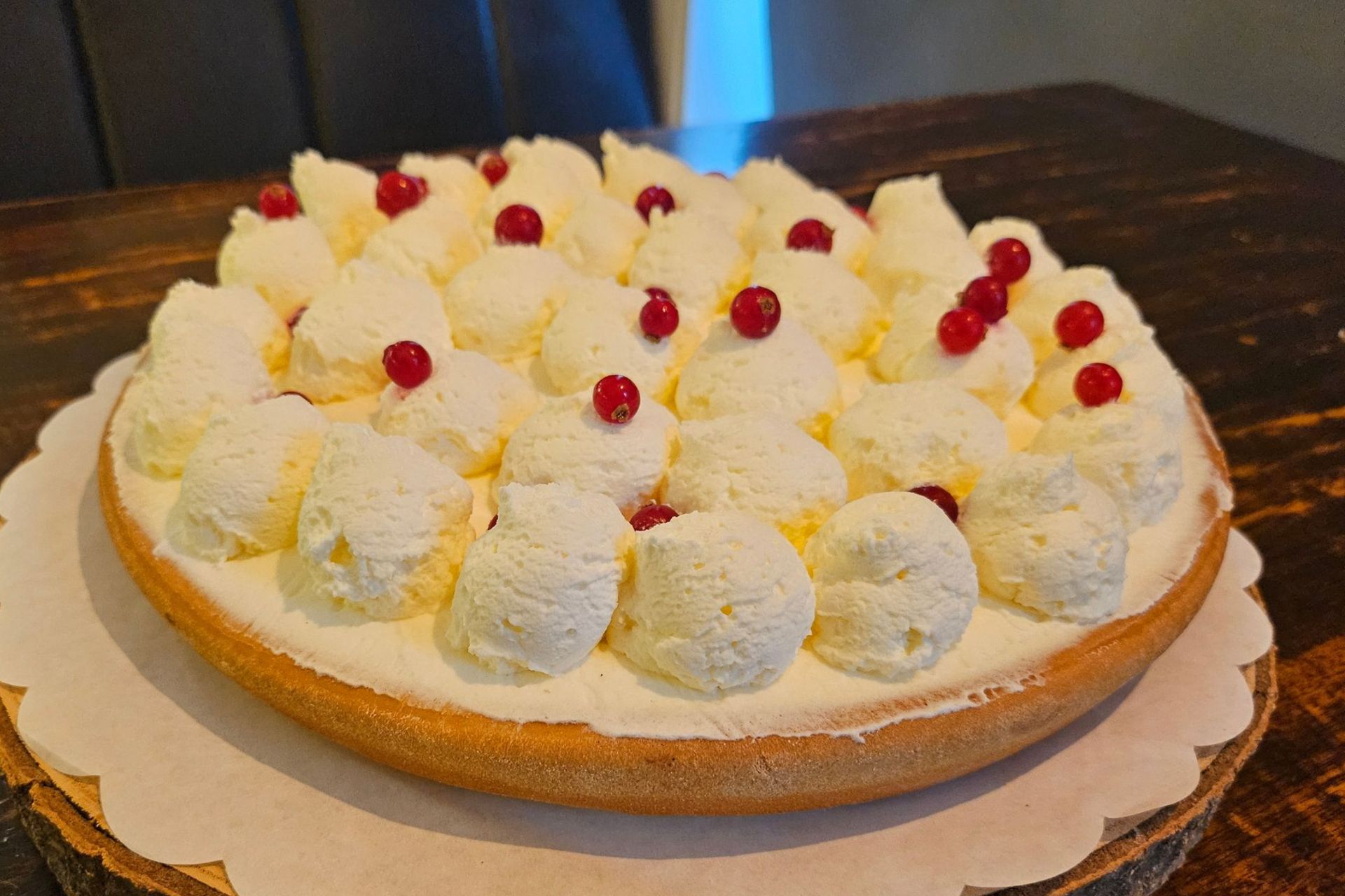 Een ronde taart, versierd met slagroomkrullen en verspreide rode bessen.