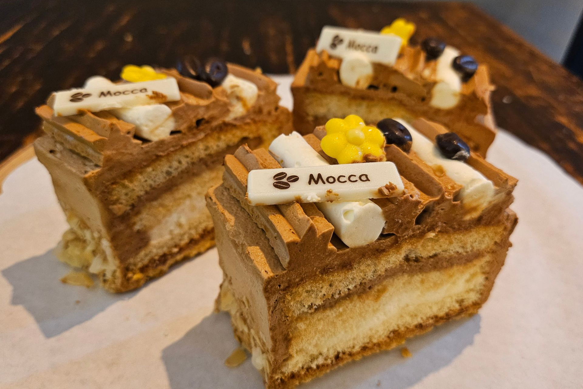 Drie rechthoekige cakes met koffiesmaak en chocoladeroom, afgewerkt met witte chocoladeplaatjes met het opschrift 