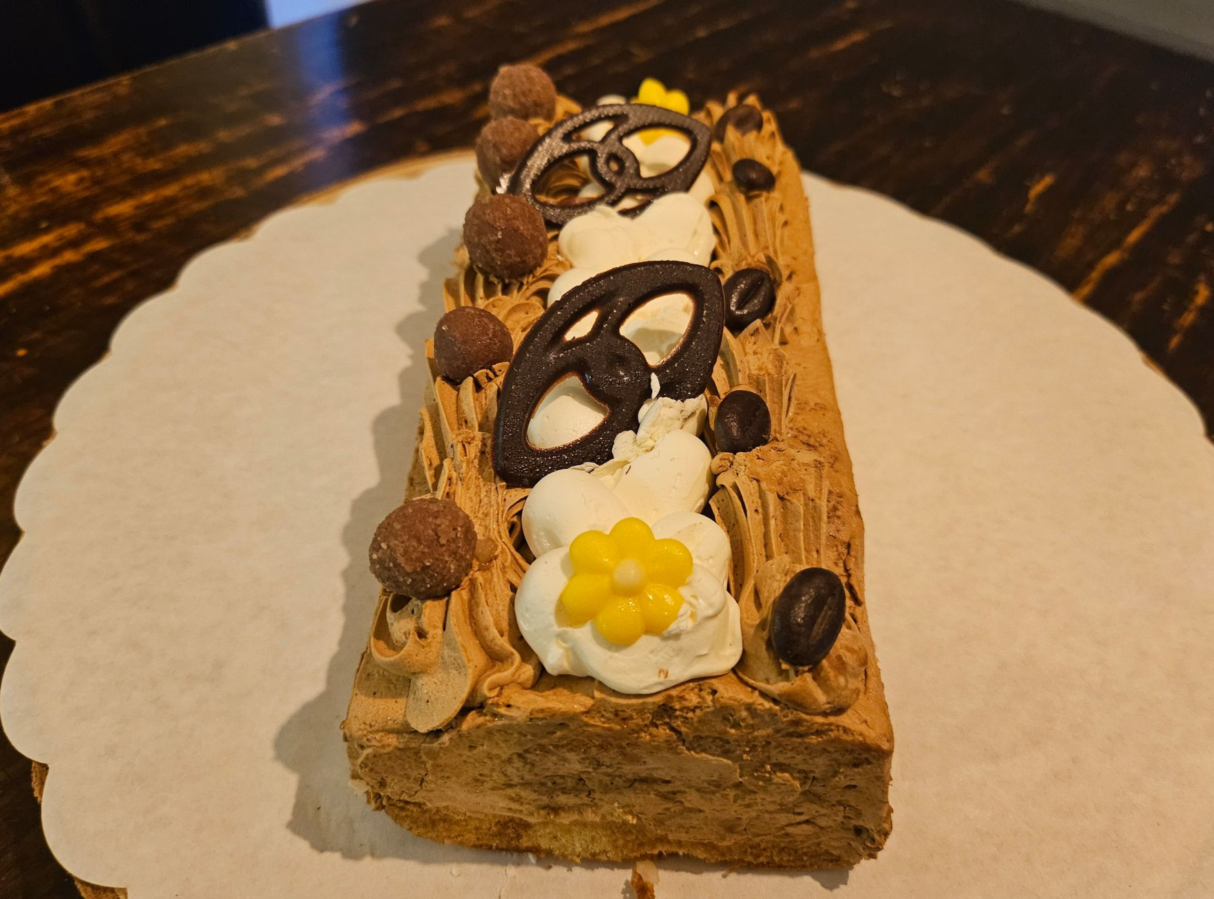 Een plakje chocoladedessert, gegarneerd met lusjes pure chocolade, truffels en een gele bloem.