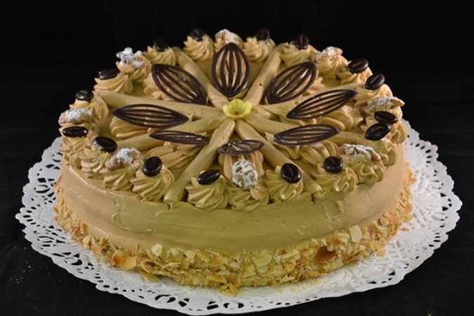 Een ronde laagjescake met koffiesmaak, versierd met spuitzakglazuur, chocoladeblaadjes en koffiebonen.