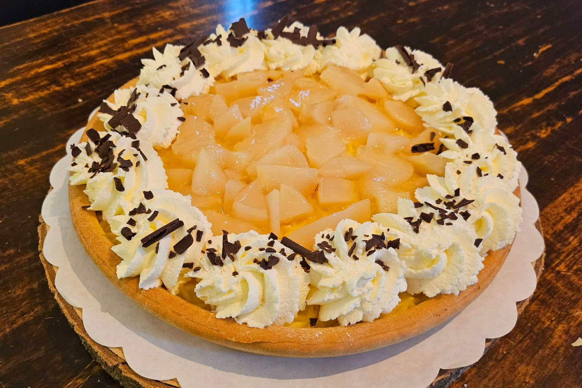 Een ronde taart, bedekt met stukjes peer, een ring van slagroomrozetten en schaafsel van pure chocolade.