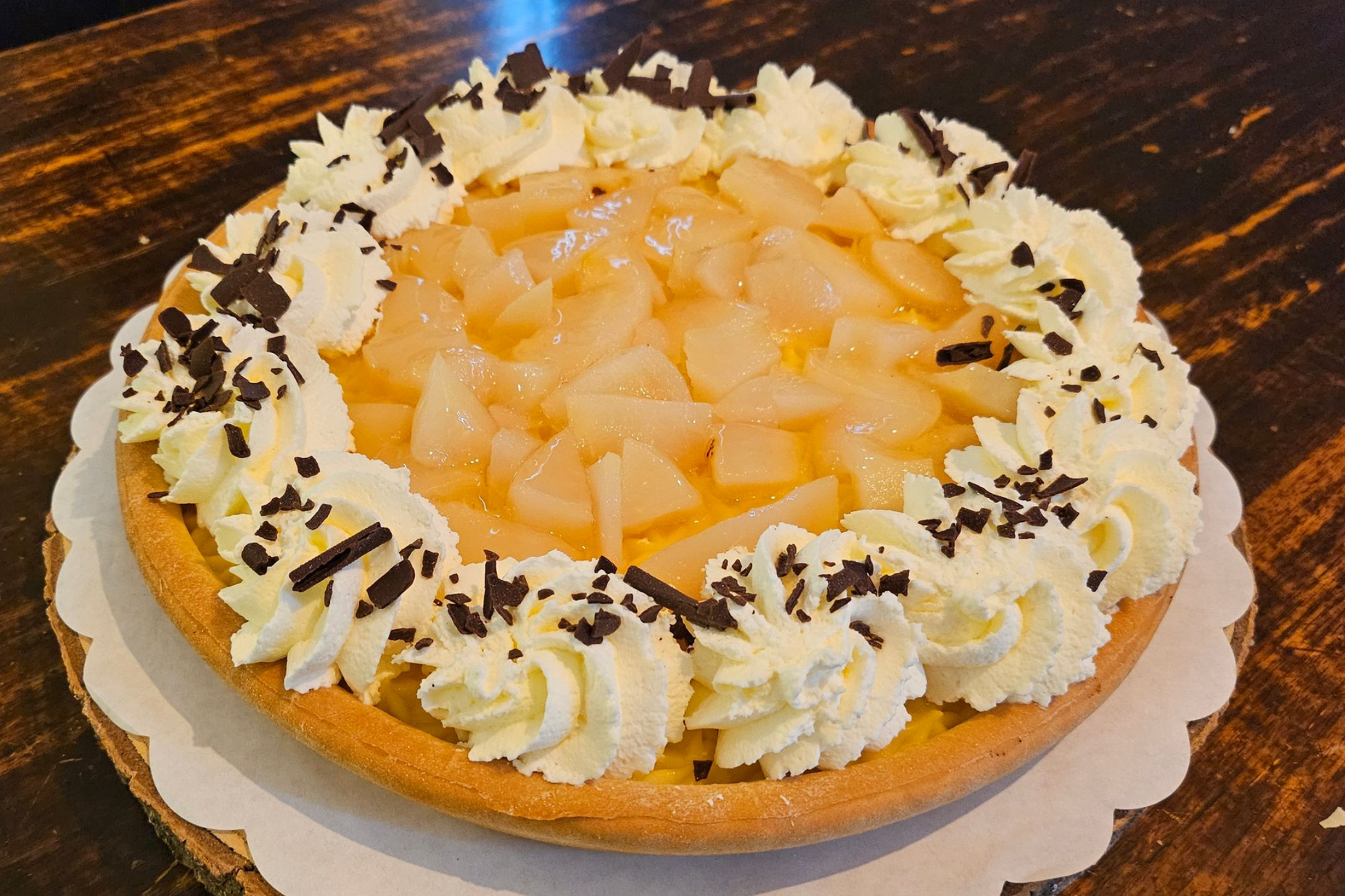 Een fruittaart met schijfjes peer, slagroomrozetten en chocoladeschaafsel.