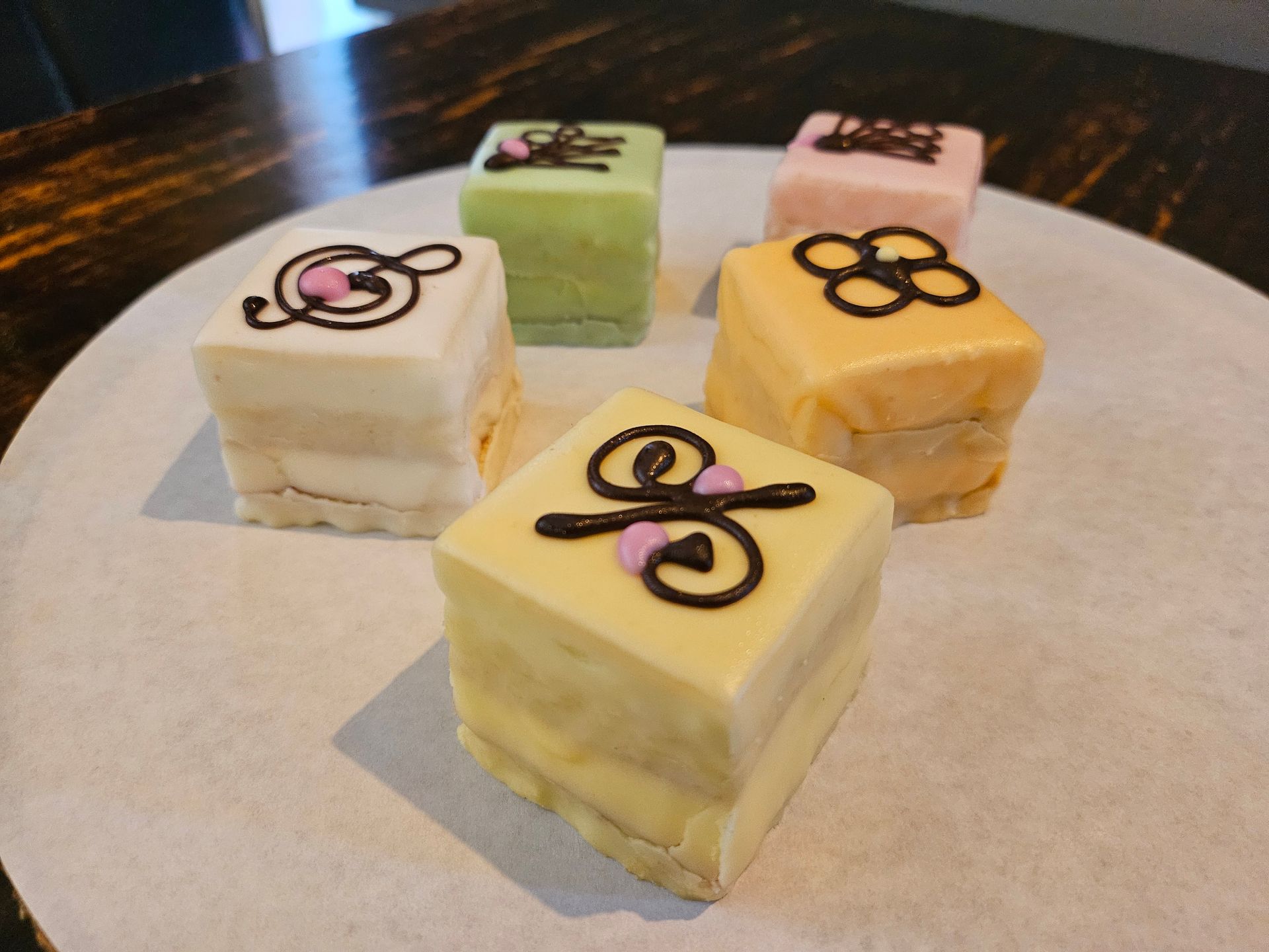 Vier kleine, versierde laagjesgebakjes in pastelkleuren..