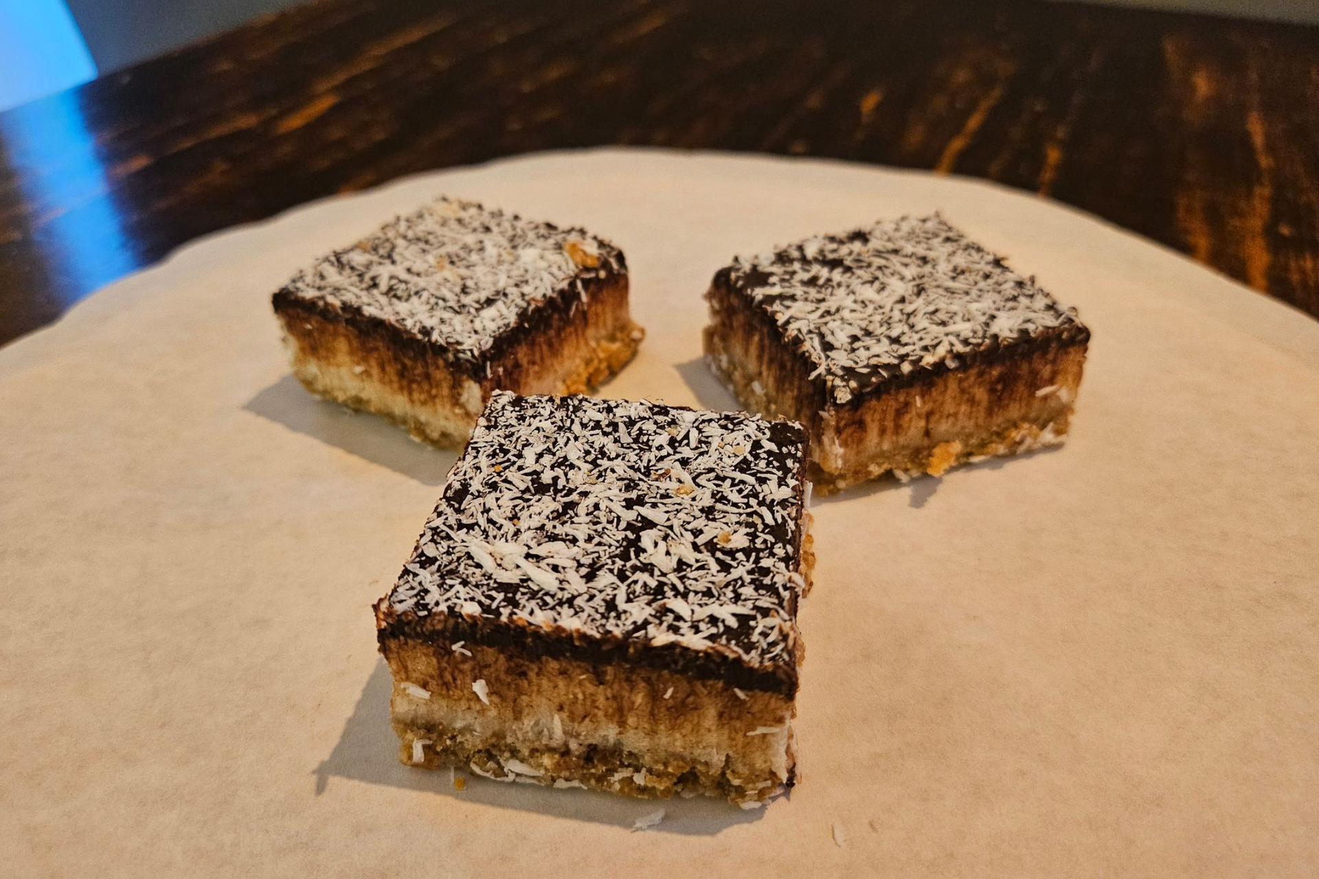 Drie vierkante, gelaagde dessertrepen, bedekt met chocolade en geraspte kokos.