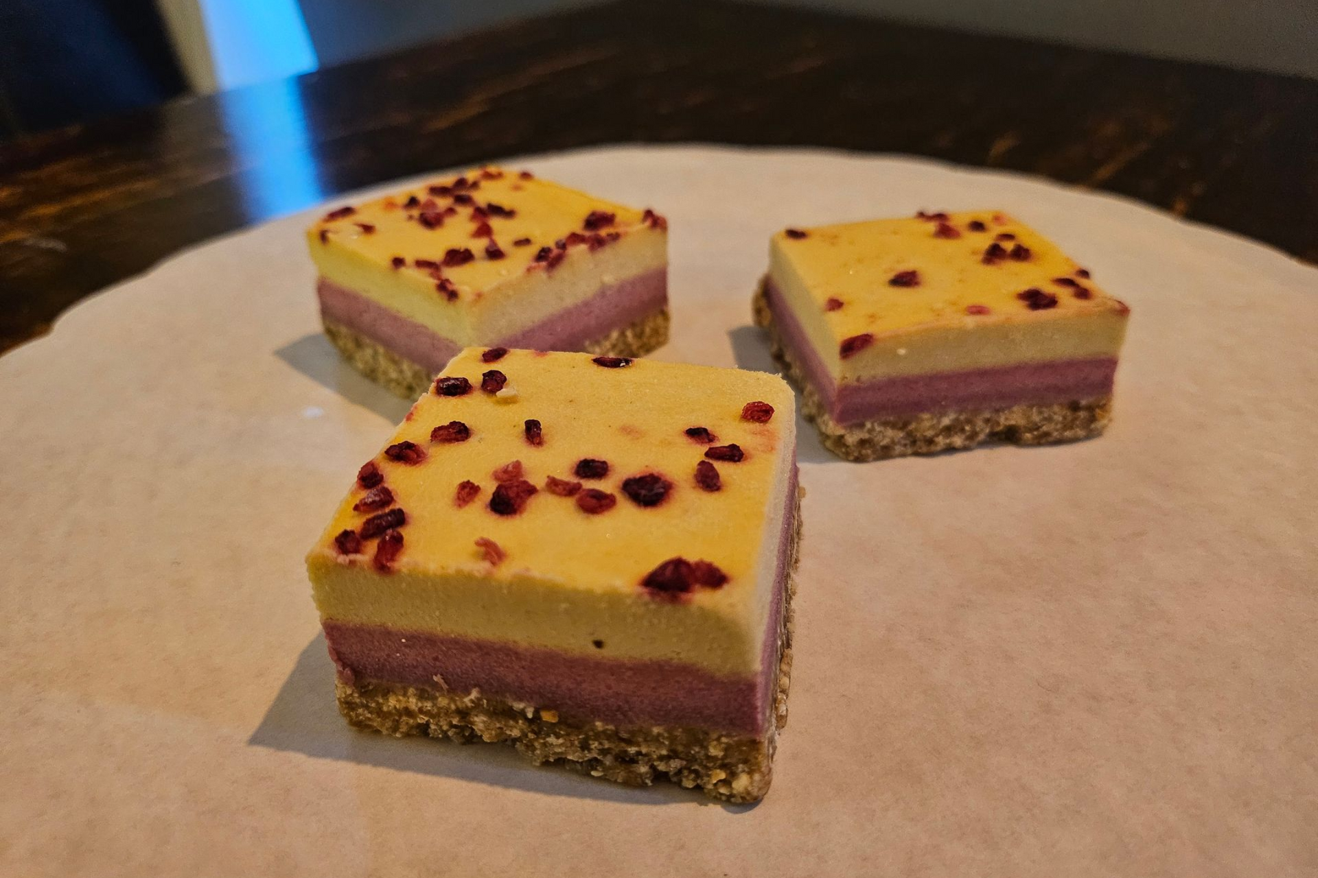 Vierkante, meerlaagse dessertrepen met een notenbodem, een bessenlaag en een gele bovenkant bestrooid met stukjes rode bessen