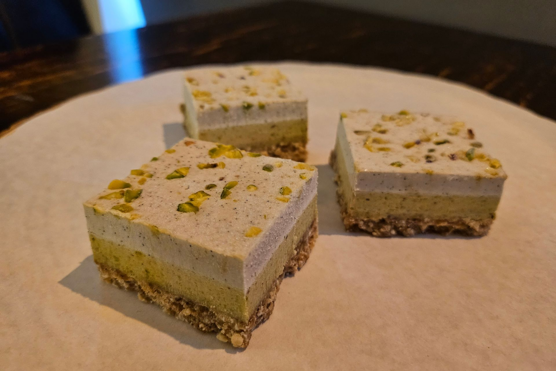 Drie vierkante, meerlaagse pistache-dessertrepen met een notenkorst.