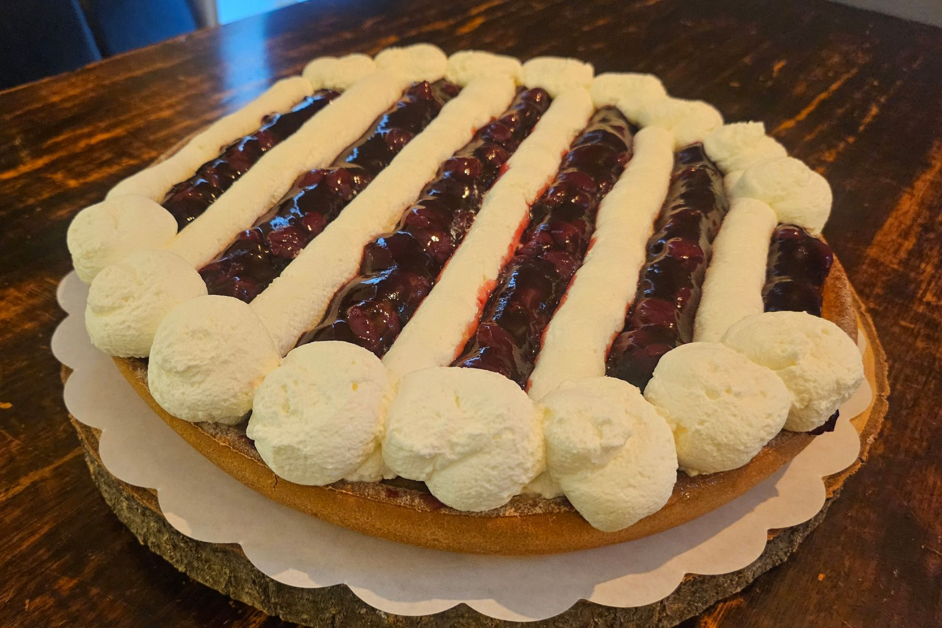 Een ronde kersentaart, versierd met strepen slagroom die over een donkerrode vruchtenvulling zijn gespoten.