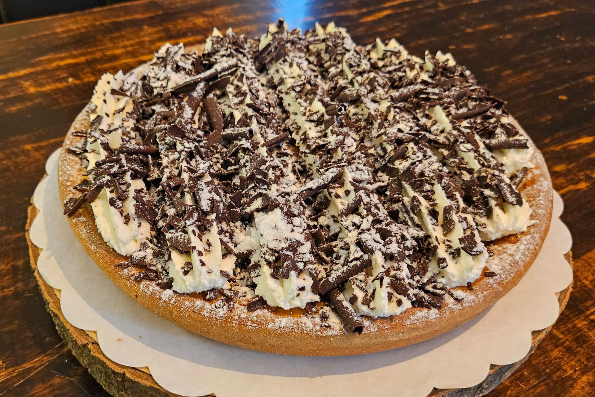 Een ronde taart, bedekt met toefjes slagroom en geschaafde pure chocolade, bestrooid met poedersuiker.