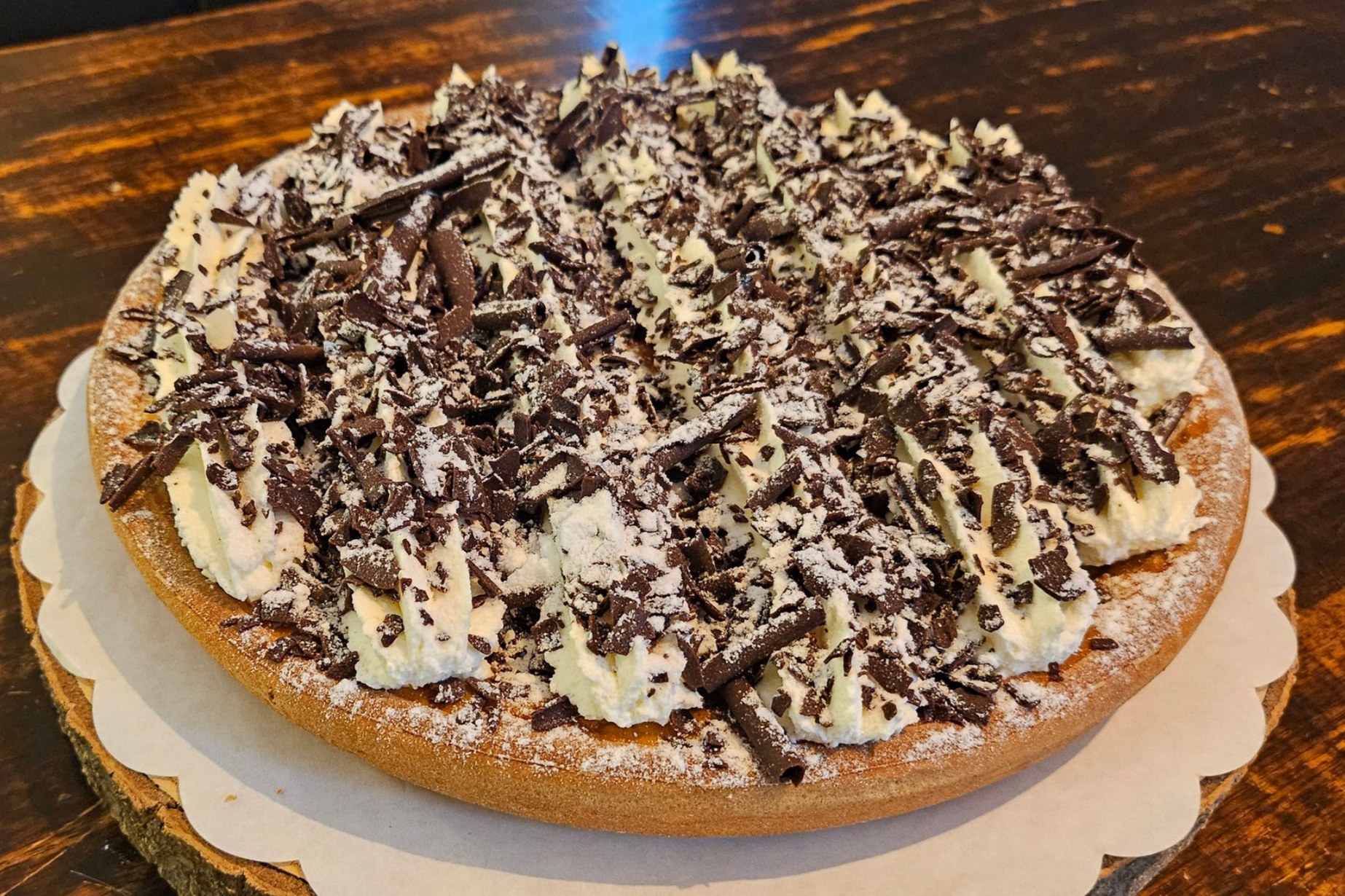 Een ronde taart, bedekt met toefjes slagroom, chocoladeschaafsel en een vleugje poedersuiker.