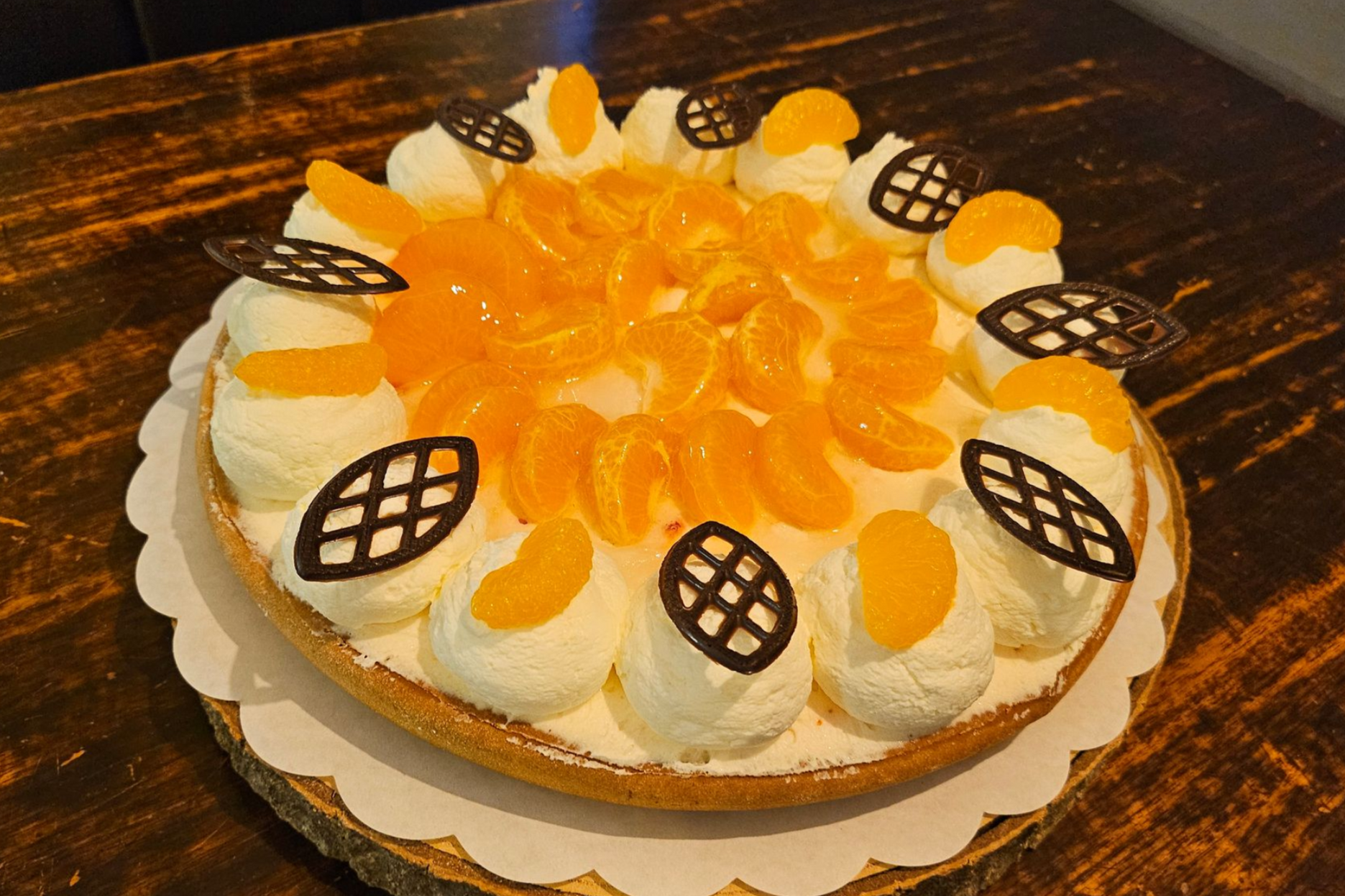 Een ronde mandarijnentaart, versierd met slagroomkrullen en decoratieve stukjes chocoladeraster.