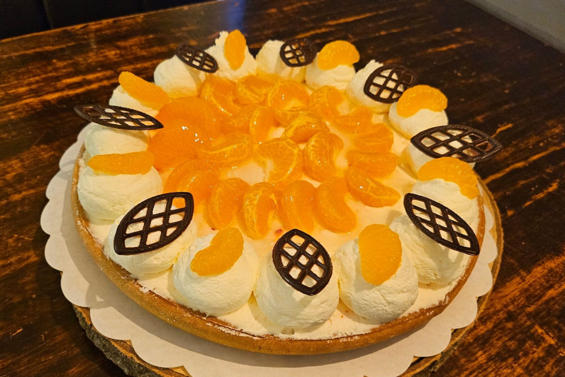 Een ronde mandarijnentaart, gegarneerd met slagroomkrullen en delicate chocoladeversieringen.