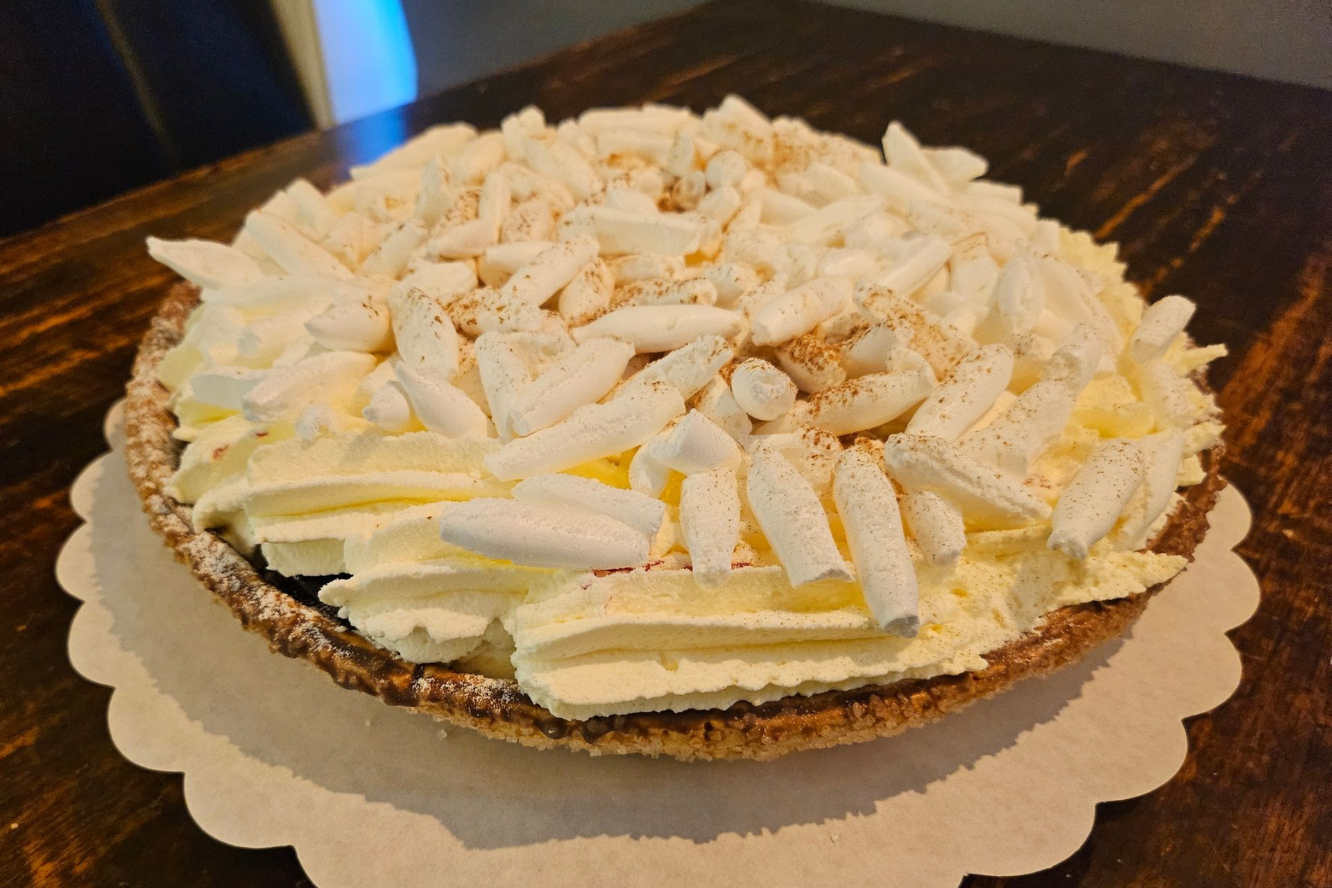 Een ronde taart, bedekt met slagroom uit een spuitzak en witte chocoladeschaafsel.