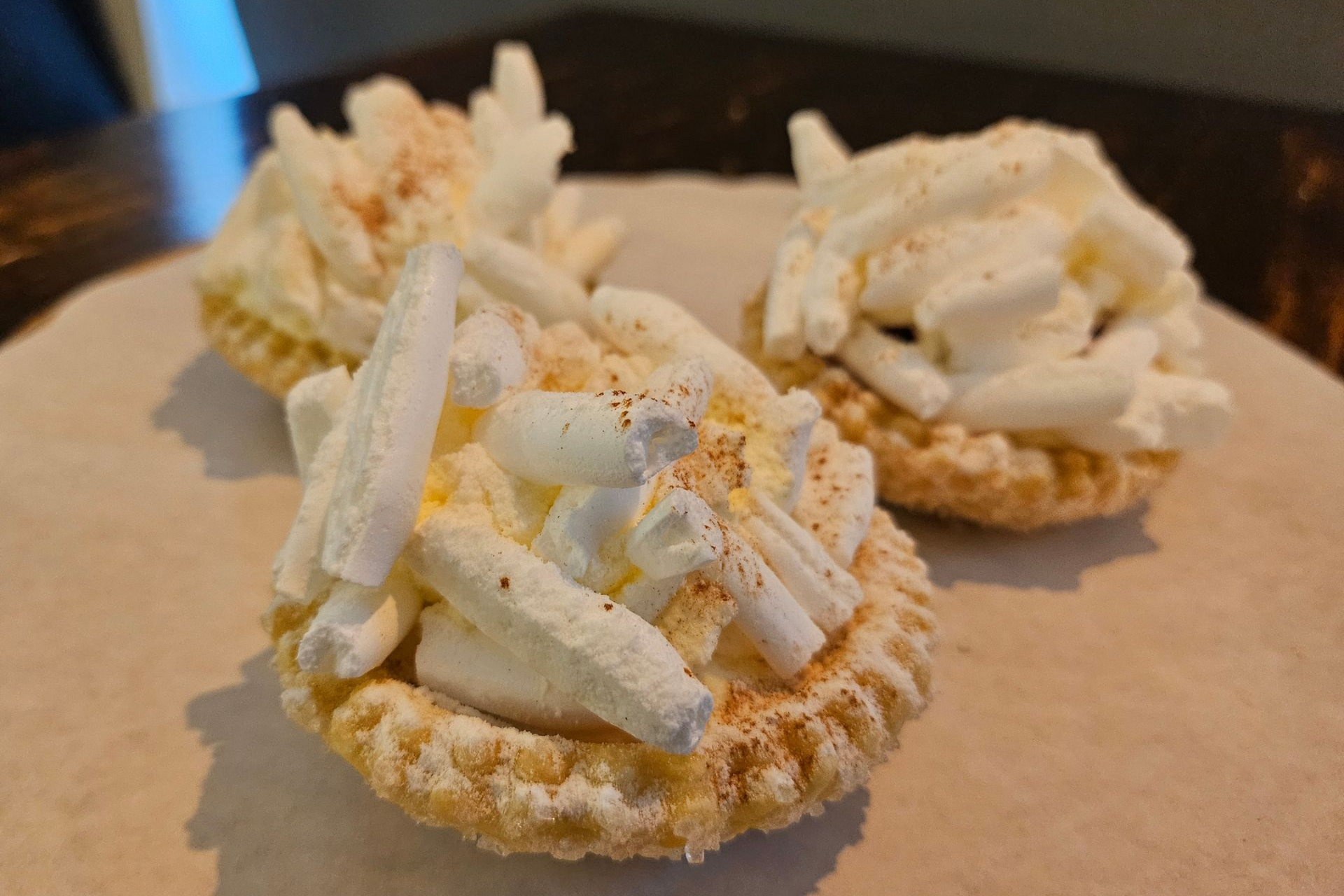 Drie kleine taartjes van bladerdeeg, gegarneerd met witte crème en bestrooid met witte schuimstaafjes.