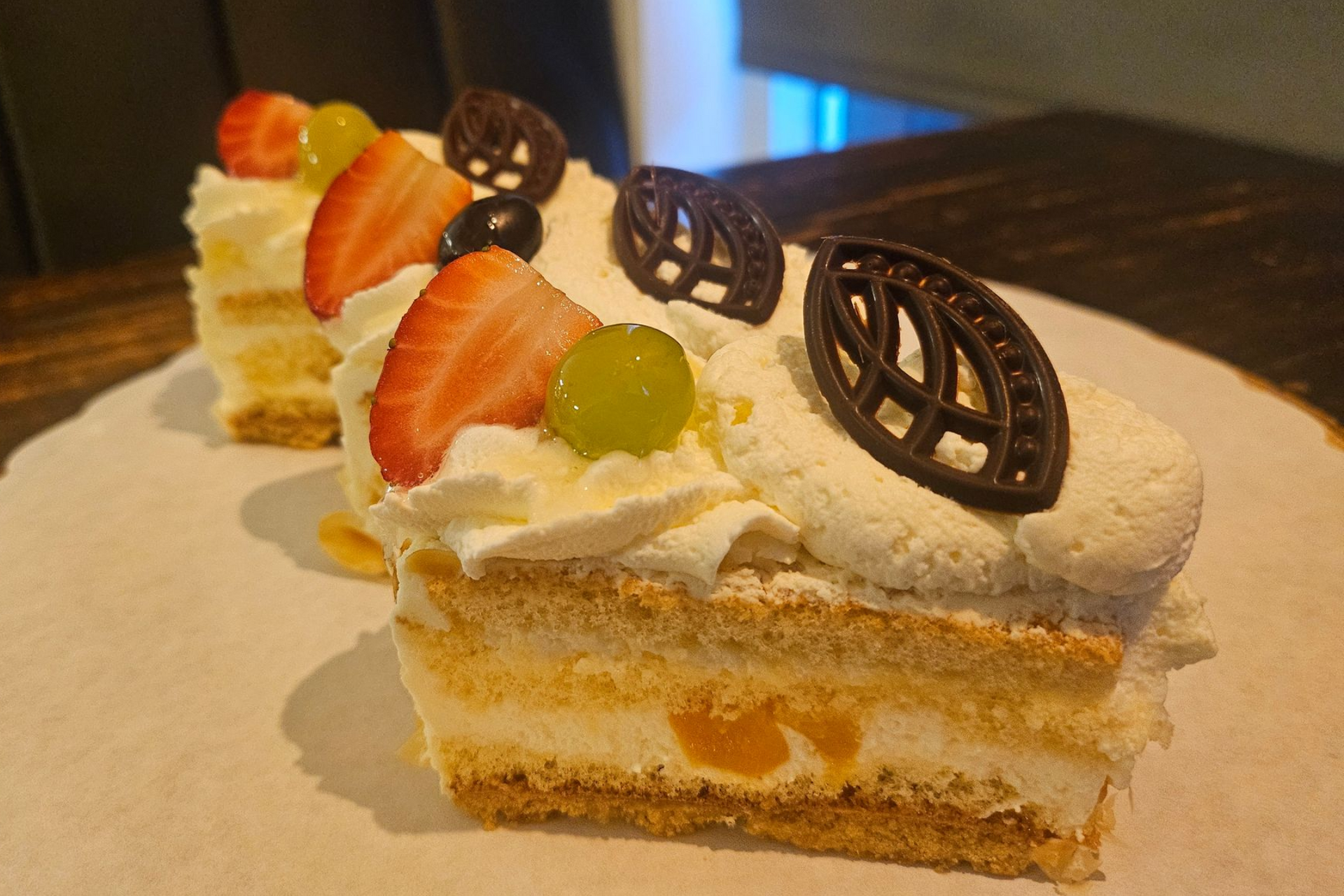 Twee plakken gelaagde cake, gegarneerd met verse aardbeien, druiven en verfijnde chocoladeversieringen.