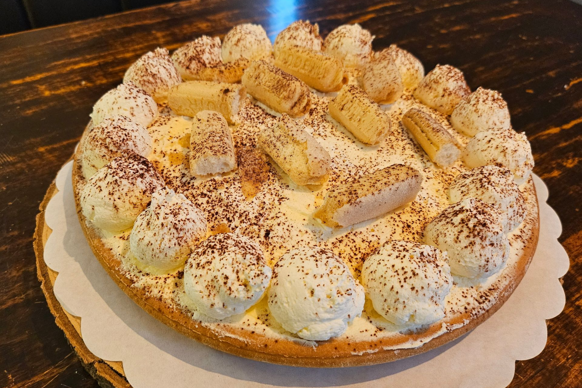 Een ronde taart, bedekt met toefjes slagroom, lange vingers en een vleugje cacaopoeder.