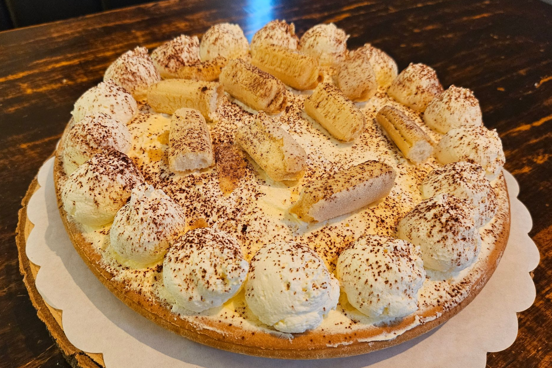 Een ronde taart, rijkelijk bedekt met slagroom, lange vingers en een vleugje cacaopoeder.