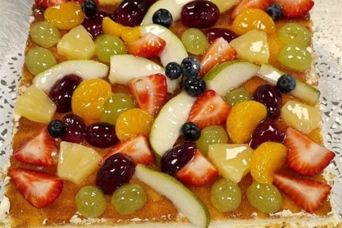 Rechthoekige fruittaart met plakjes aardbeien, druiven, mandarijnen, ananas en bessen op een romige bodem.