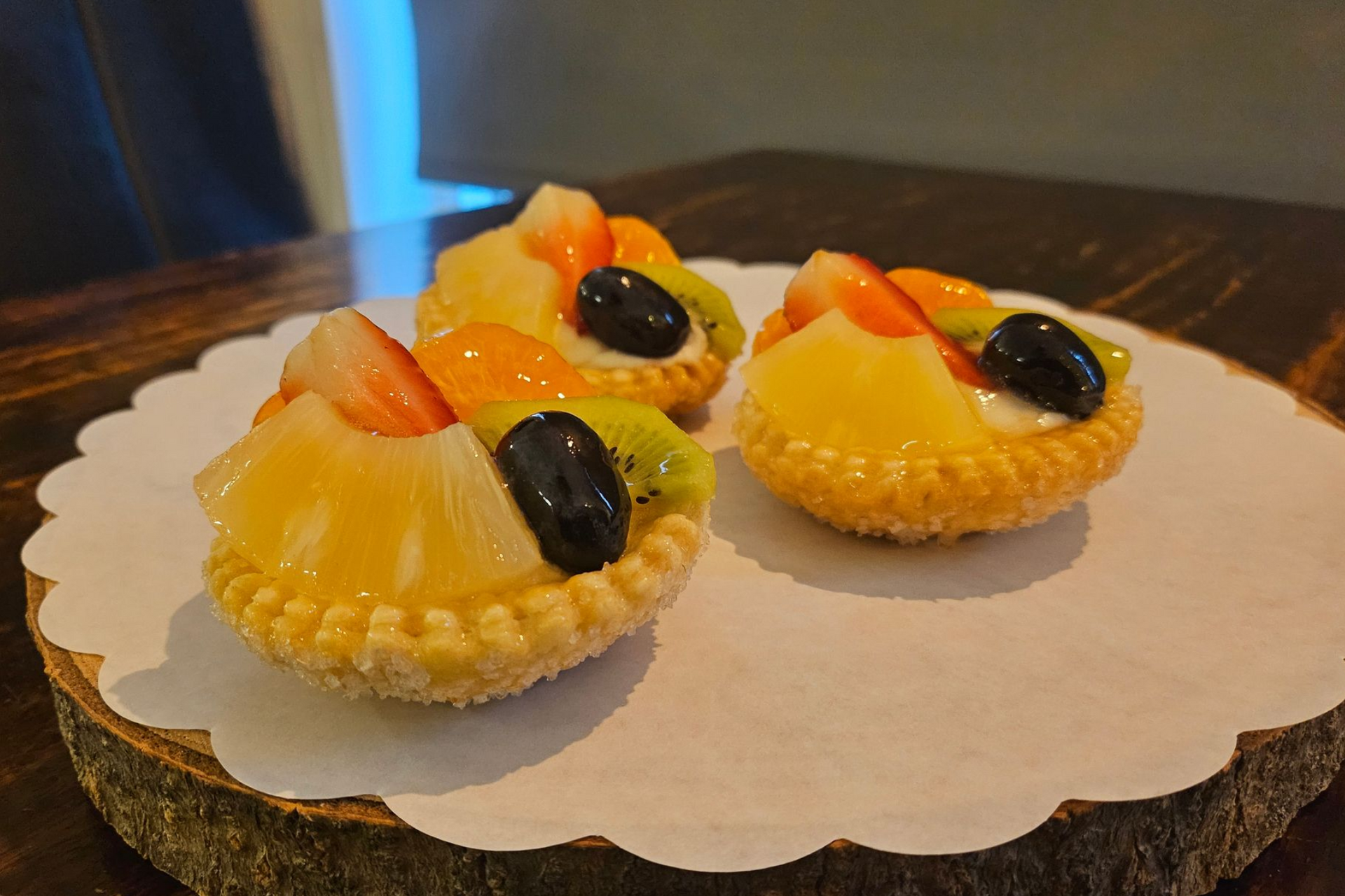 Drie kleine fruittaartjes met aardbeien, ananas, kiwi en druiven.