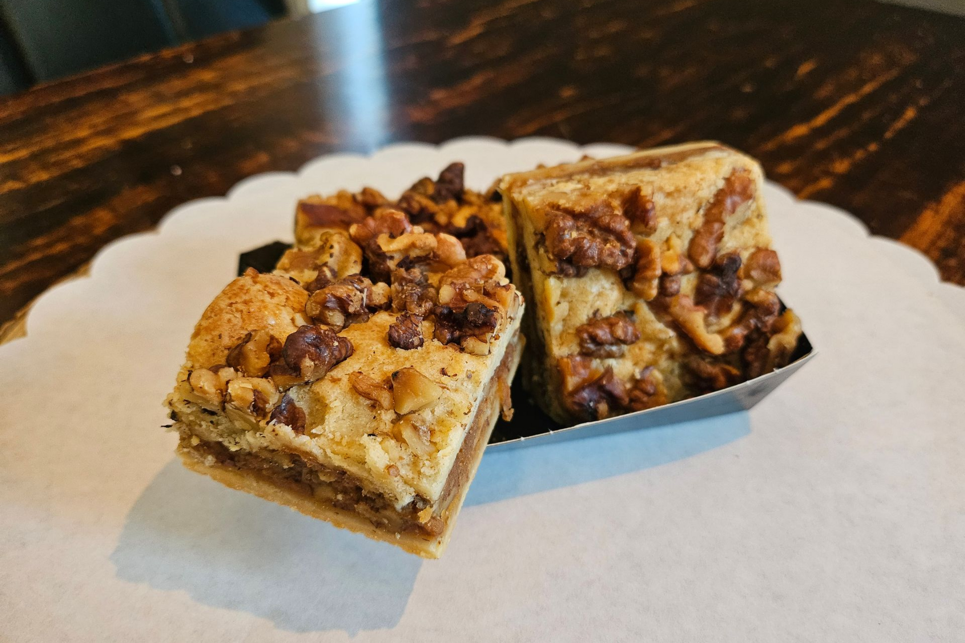 Twee vierkante dessertrepen met walnoten en karamel, geserveerd in een klein papieren schaaltje.