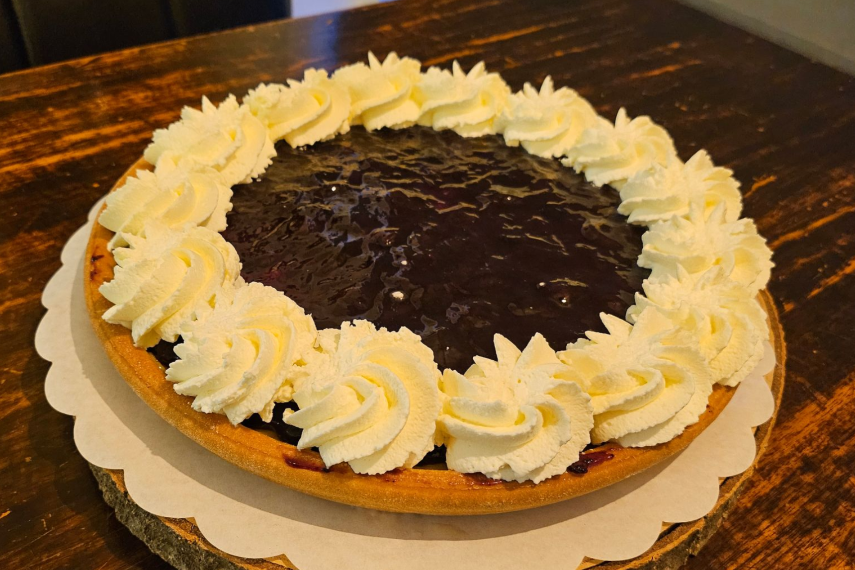 Een ronde bosbessentaart met een donkerpaarse fruitvulling, omrand met slagroom.