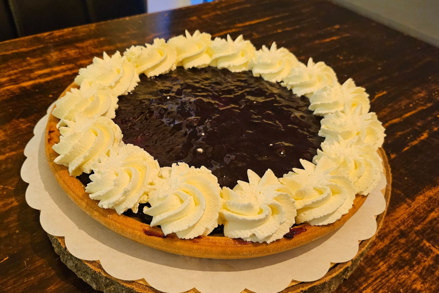 Een taart met een donkerpaarse vruchtenvulling en een rand van opgespoten slagroomkrullen.