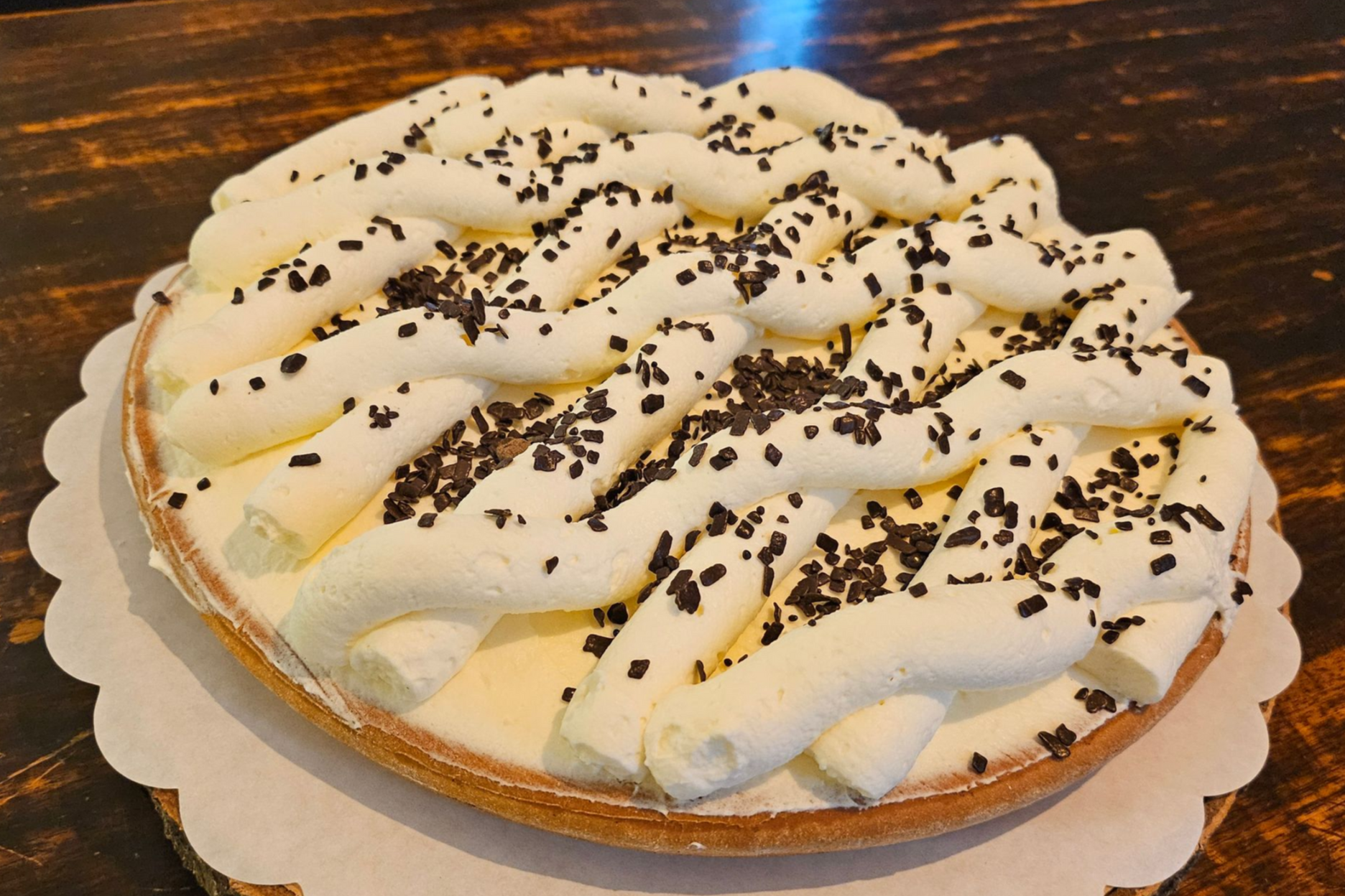 Een ronde taart, bedekt met een rasterpatroon van witte room en bestrooid met geschaafde pure chocolade.