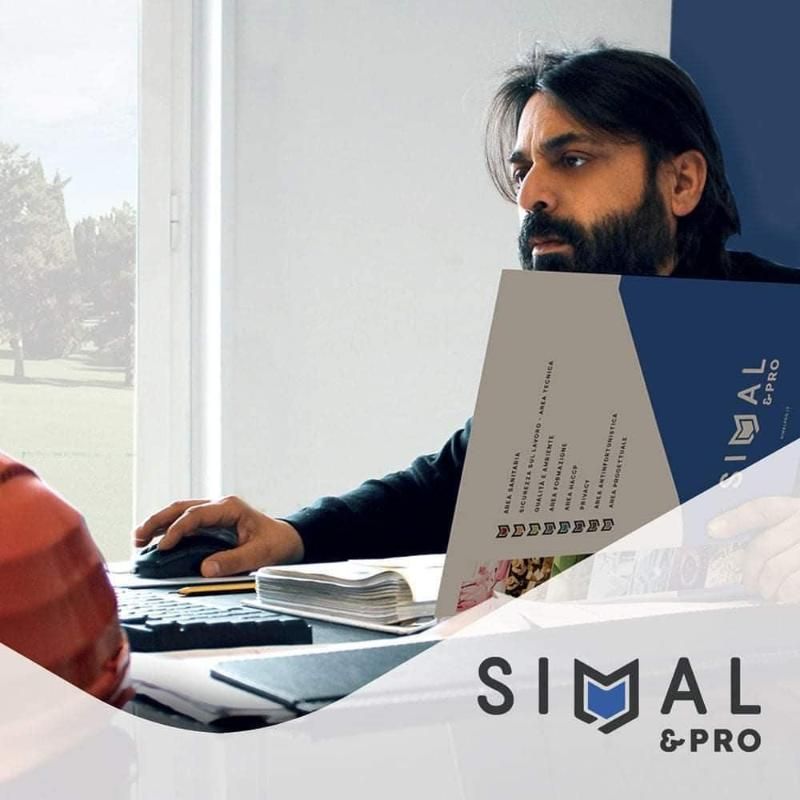 Un uomo lavora a una scrivania con un computer portatile e un notebook accanto a una brochure di Simal Pro.