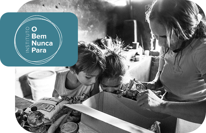 A woman with two children opening a box of groceries offered by the Instituto O Bem Nunca Para.