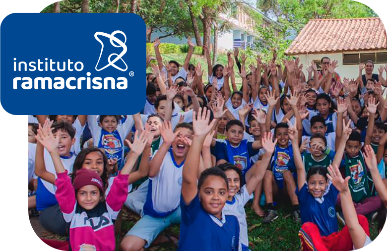Um grupo de mais de trinta crianças do Instituto Ramacrisna sorrindo com os braços levantados para cima.