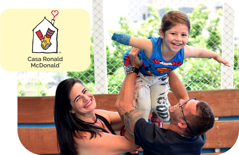 Uma mulher e um homem segurando para cima um menino com deficiência sorridente representando a Casa Ronald McDonald.
