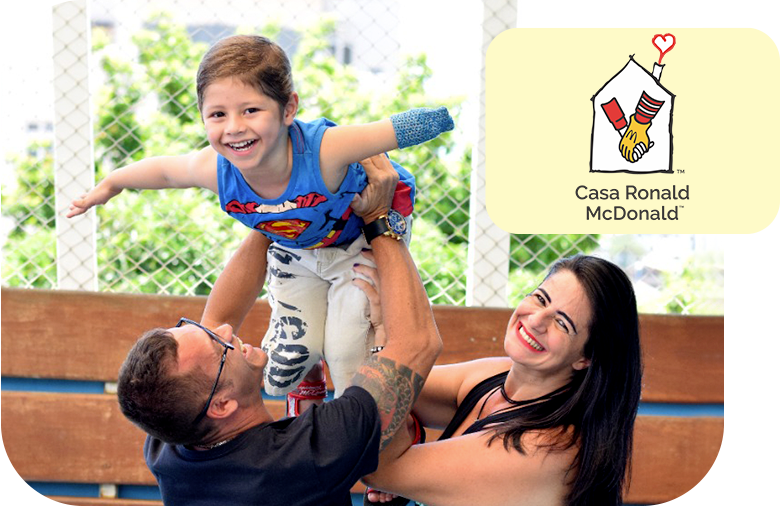 A woman and a man holding a smiling boy with a disability and a sign representing the Ronald McDonald House.