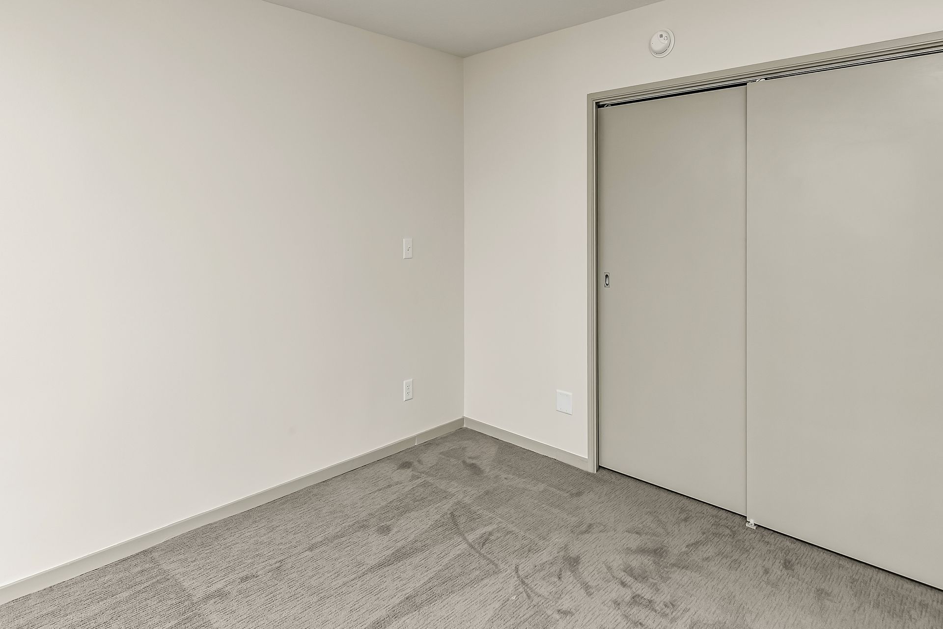 Empty carpeted bedroom with white walls and sliding closet doors