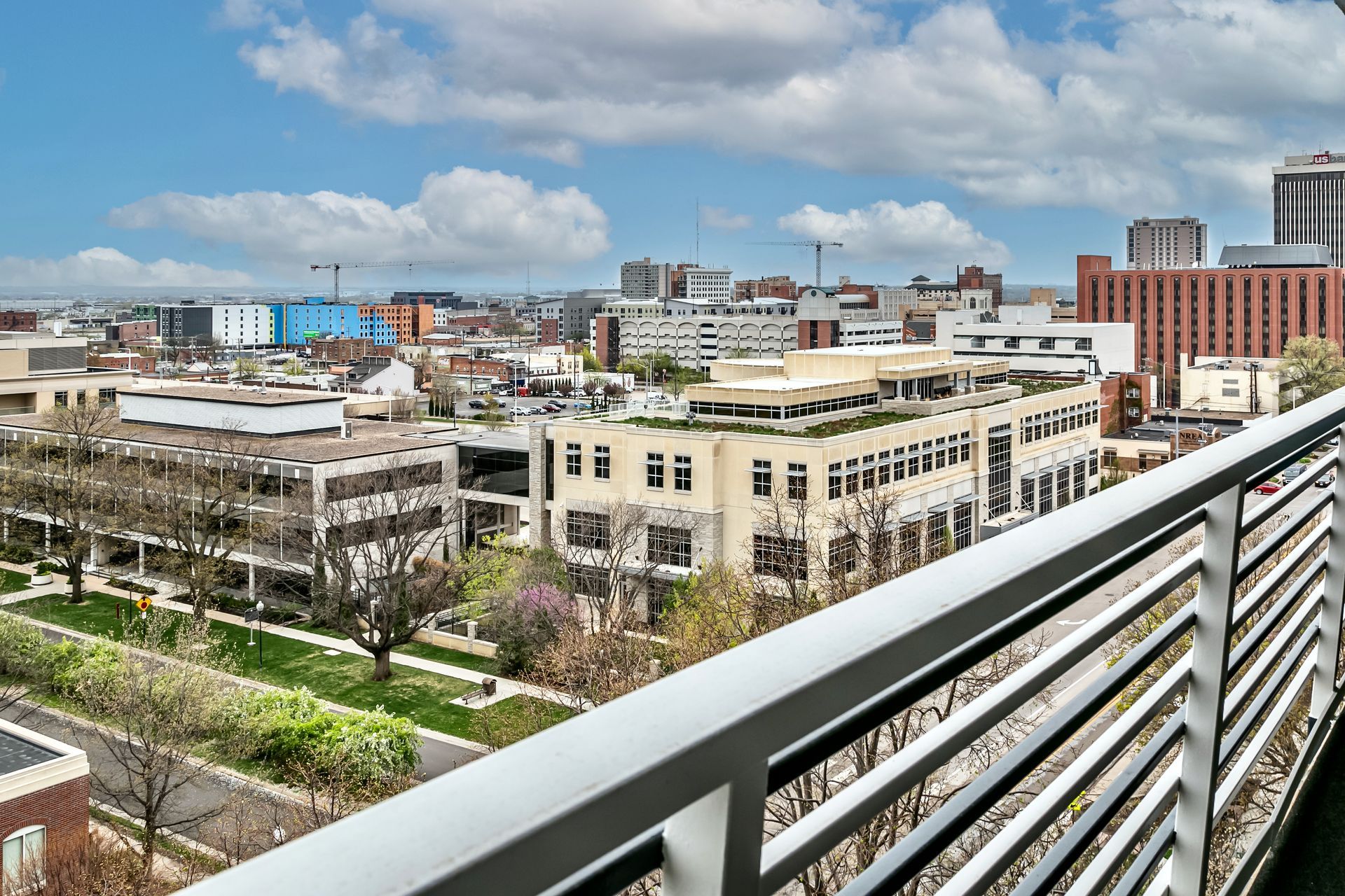 City skyline viewed from a balcony with metal railing under a bright, cloudy sky