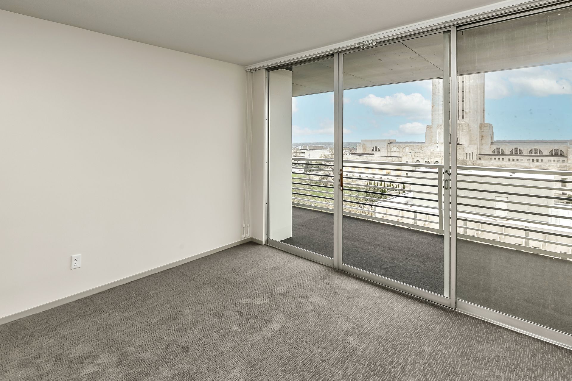 Empty carpeted room with sliding glass doors opening to a balcony and city view