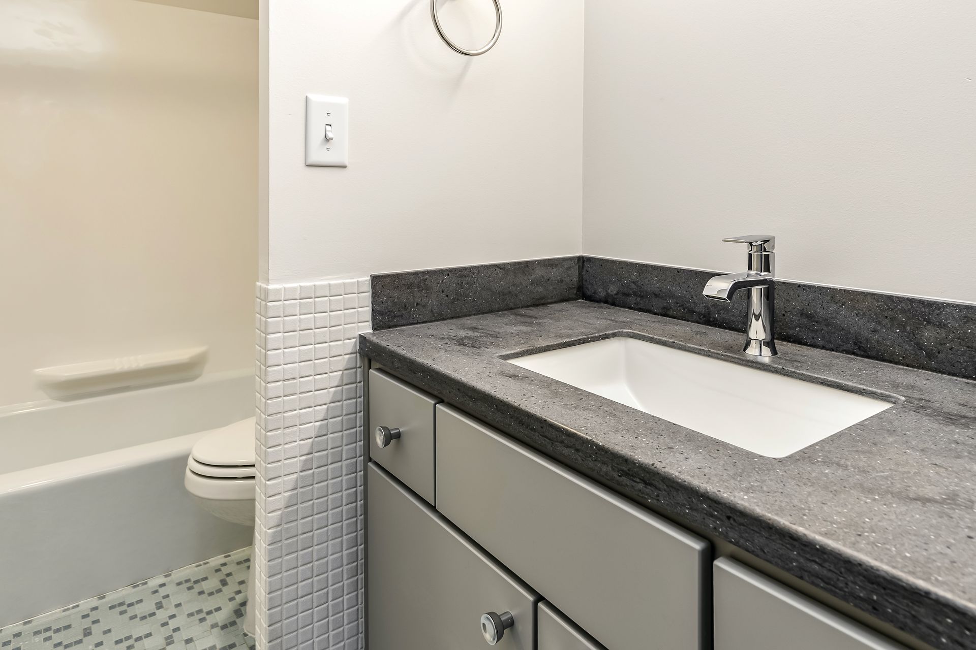 Bathroom vanity with white sink, dark granite countertop, and tub area in the background.