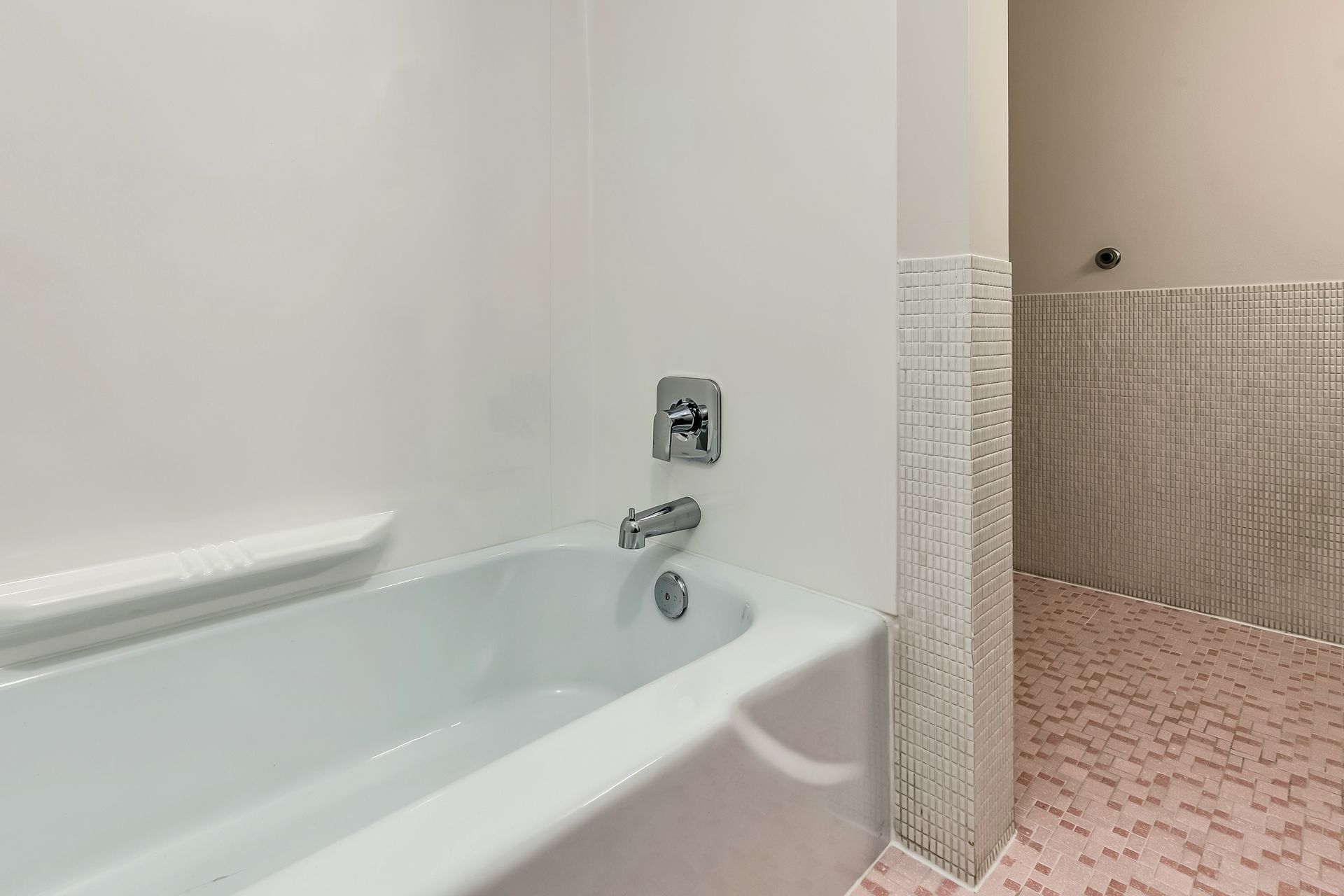 Bathroom with white bathtub, chrome faucet, and beige-tiled shower area with pink floor tiles.