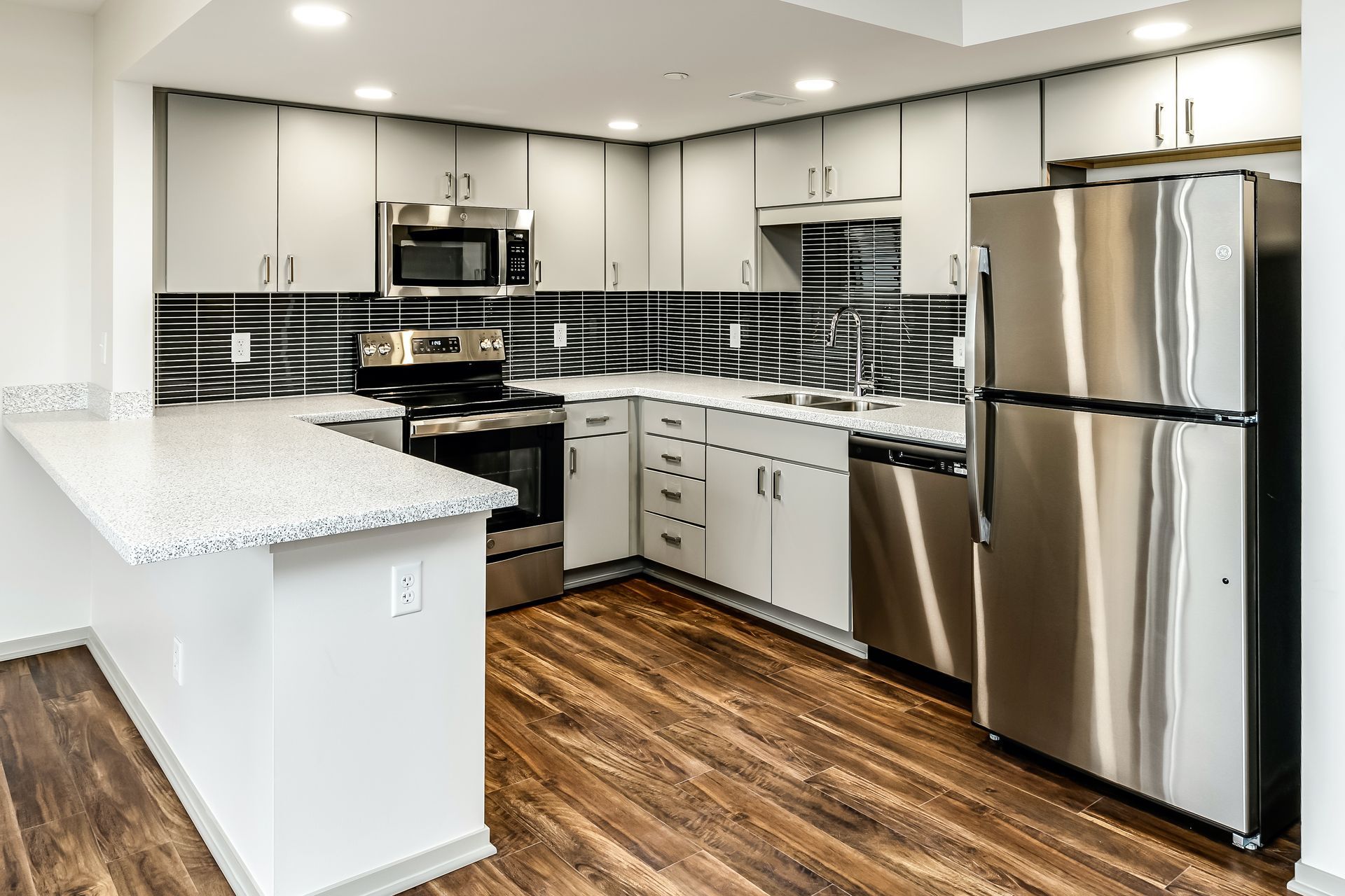 Modern kitchen with stainless steel appliances, white cabinets, black tile backsplash, and wood flooring