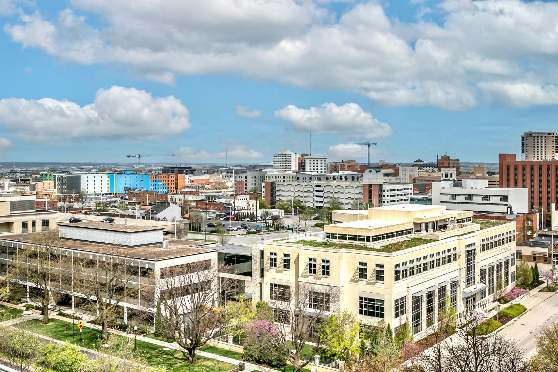Aerial view of a cityscape with modern buildings under a blue sky with scattered clouds.