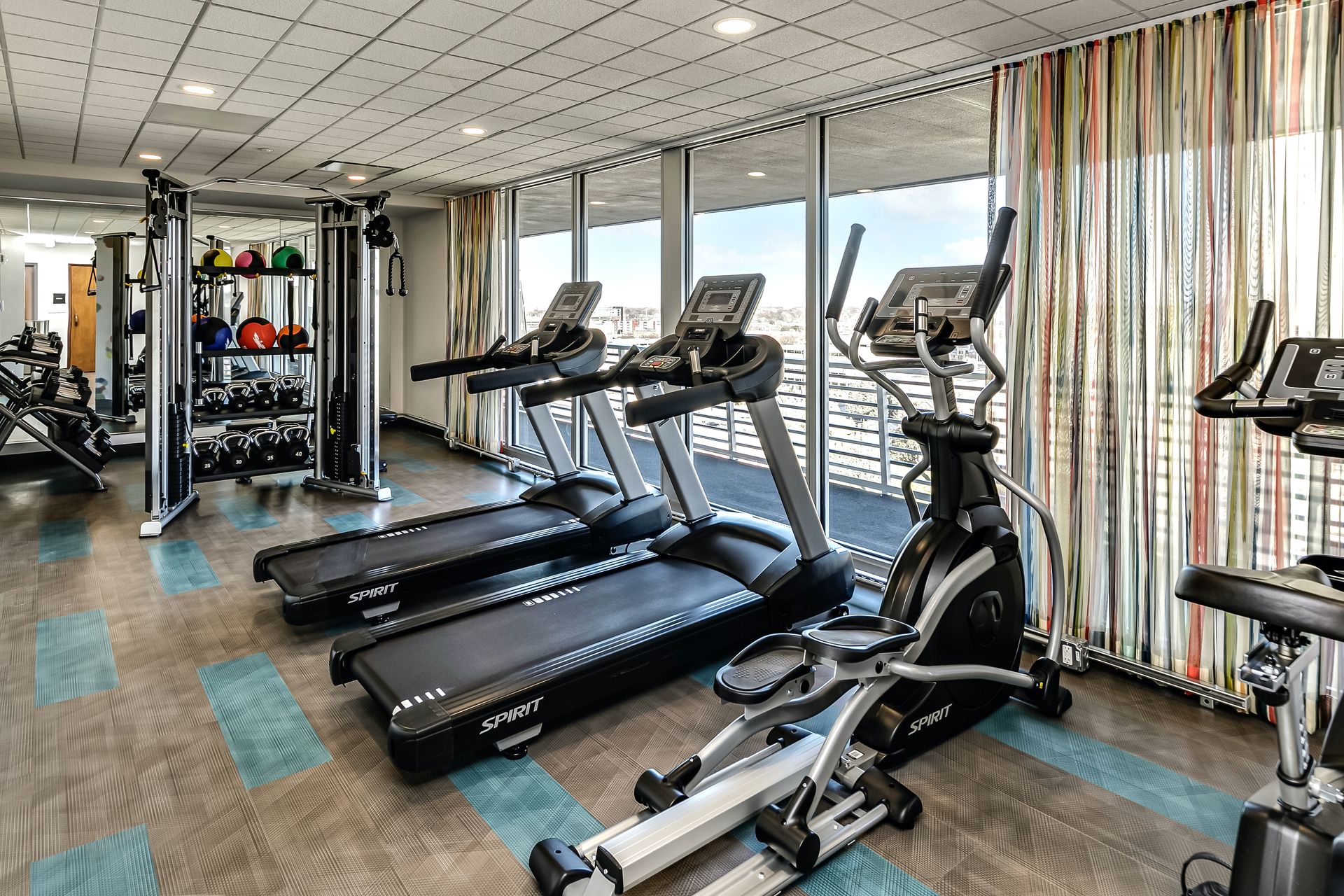 Modern gym with treadmills, ellipticals, and large windows overlooking the city