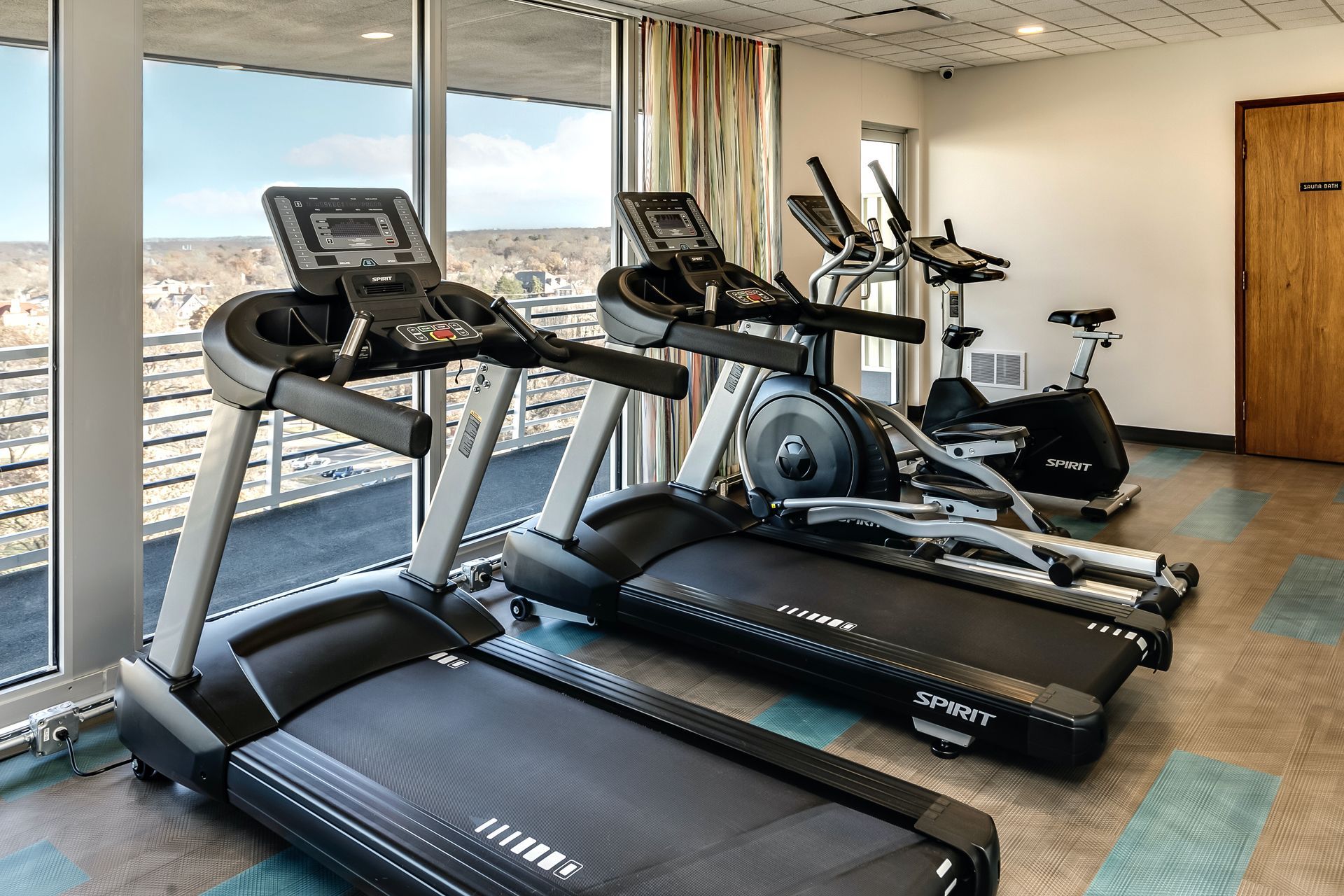 Gym with treadmills and an elliptical by large windows overlooking a city view